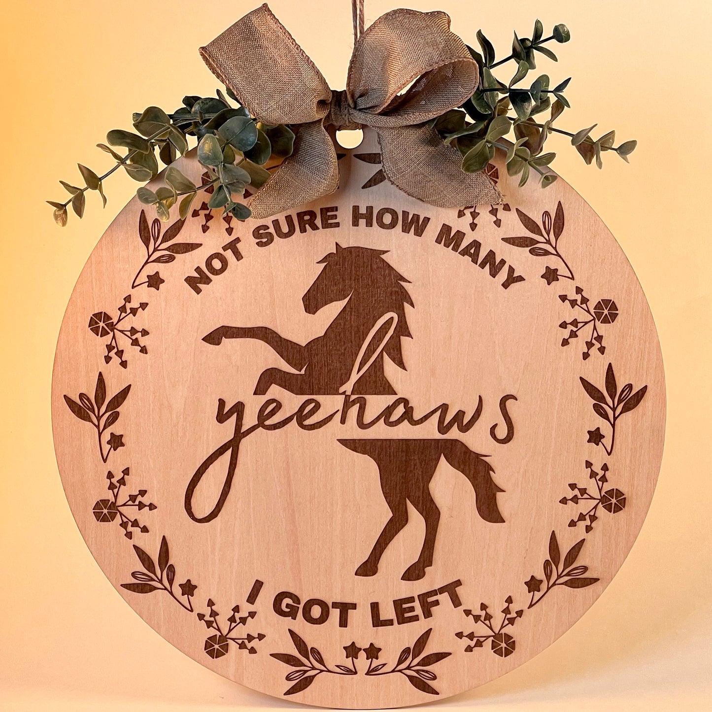 Laser-engraved wood sign featuring 'Not Sure How Many Yeehaws I Got Left,' decorated with a horse silhouette, floral accents, and a rustic bow.