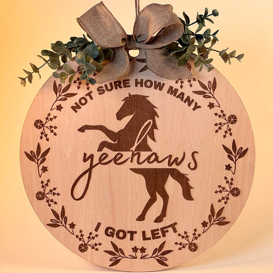 Laser-engraved wood sign featuring 'Not Sure How Many Yeehaws I Got Left,' decorated with a horse silhouette, floral accents, and a rustic bow.