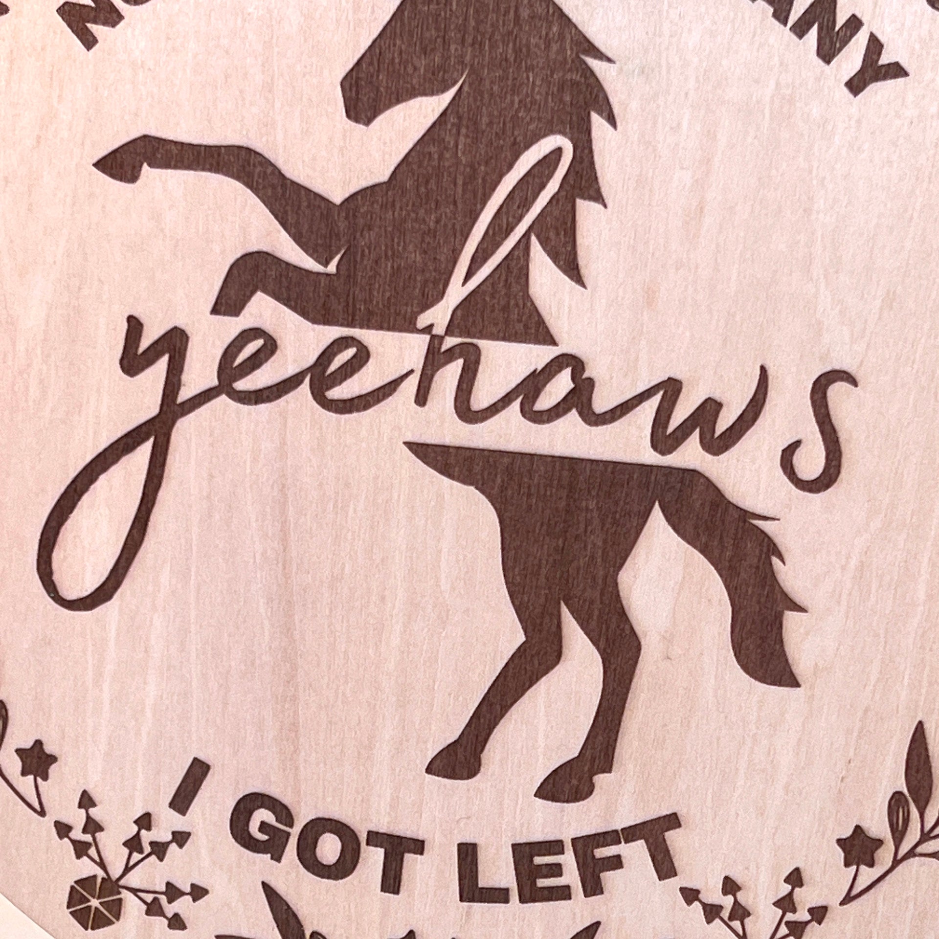 Laser-engraved wood sign featuring 'Not Sure How Many Yeehaws I Got Left,' decorated with a horse silhouette, floral accents, and a rustic bow.