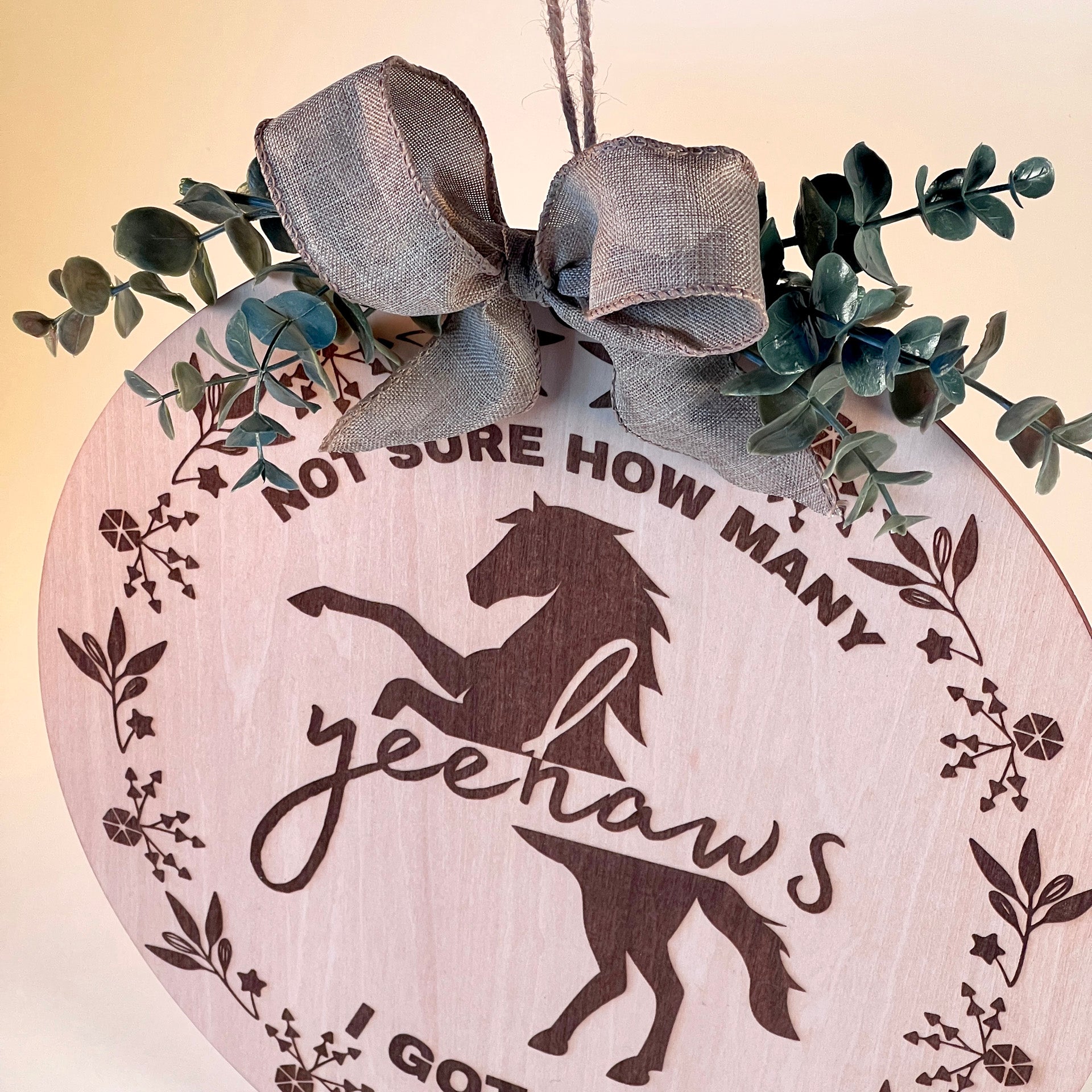 Laser-engraved wood sign featuring 'Not Sure How Many Yeehaws I Got Left,' decorated with a horse silhouette, floral accents, and a rustic bow.