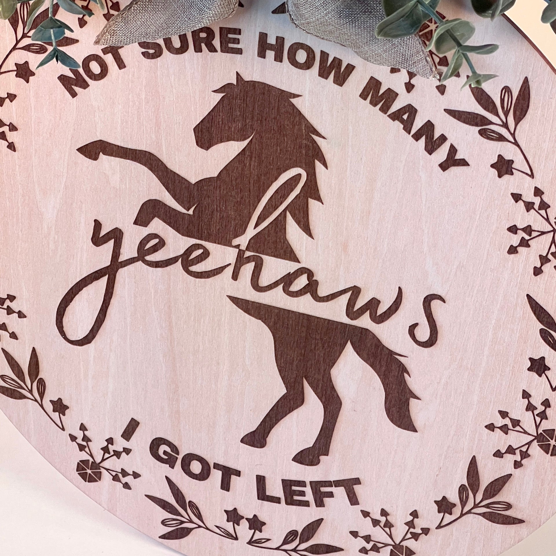 Laser-engraved wood sign featuring 'Not Sure How Many Yeehaws I Got Left,' decorated with a horse silhouette, floral accents, and a rustic bow.
