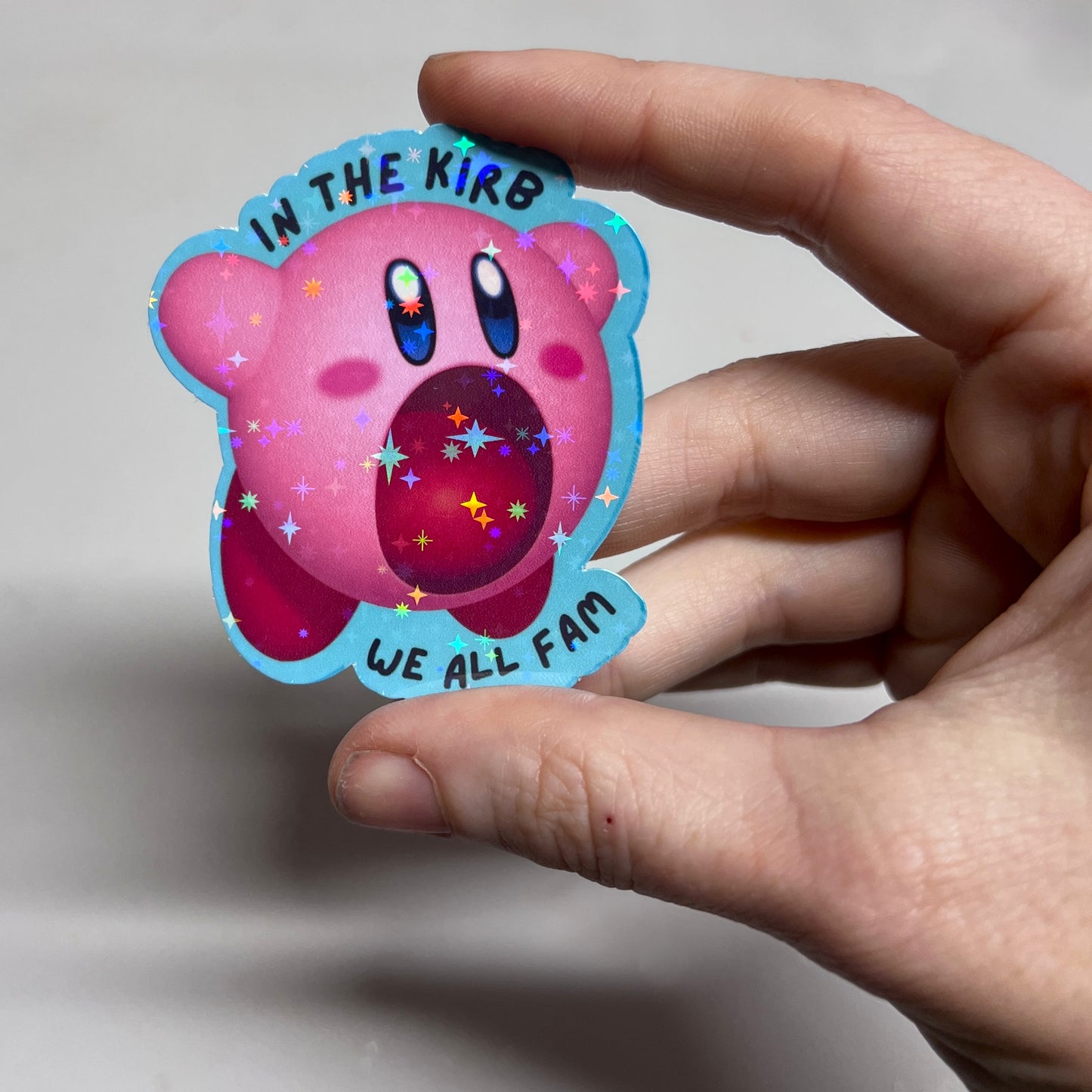 Holographic vinyl sticker featuring a cute Kirby with the phrase "In the Kirb, We All Fam." Perfect for laptops, water bottles, or gamer gear.