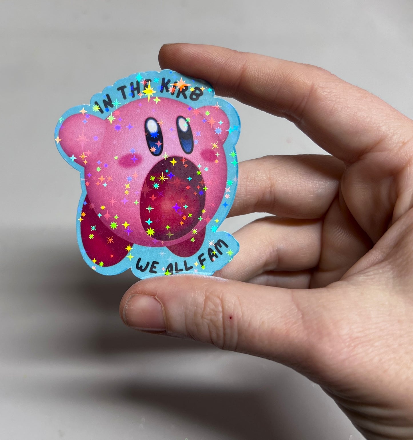 Holographic vinyl sticker featuring a cute Kirby with the phrase "In the Kirb, We All Fam." Perfect for laptops, water bottles, or gamer gear.