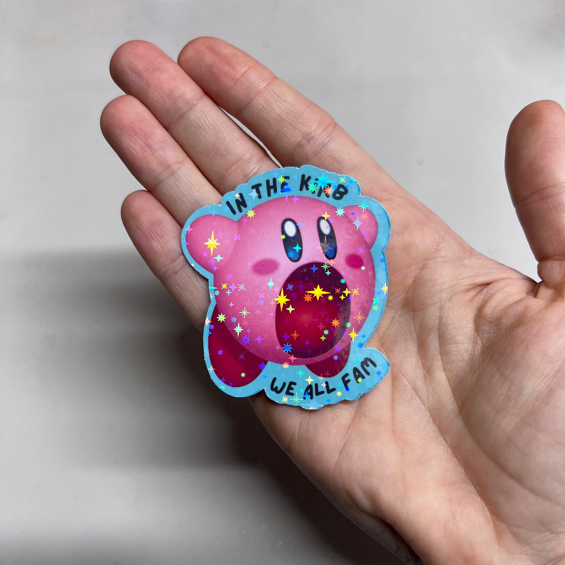 Holographic vinyl sticker featuring a cute Kirby with the phrase "In the Kirb, We All Fam." Perfect for laptops, water bottles, or gamer gear.