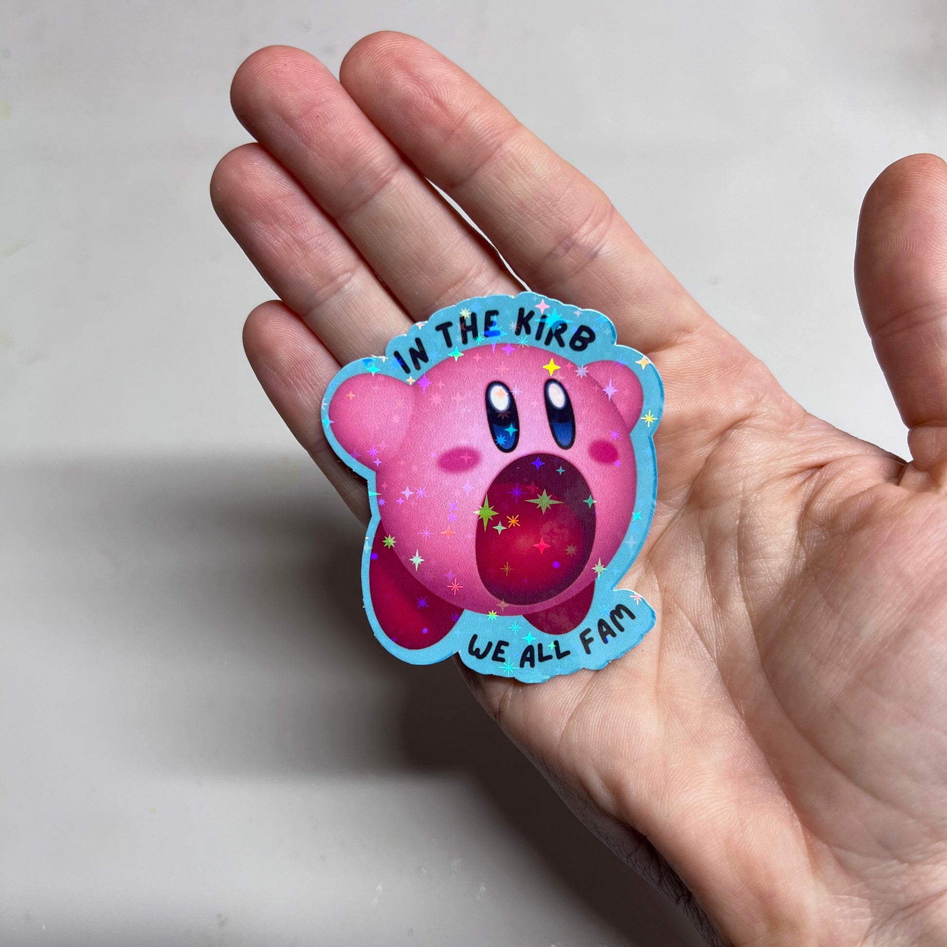 Holographic vinyl sticker featuring a cute Kirby with the phrase "In the Kirb, We All Fam." Perfect for laptops, water bottles, or gamer gear.