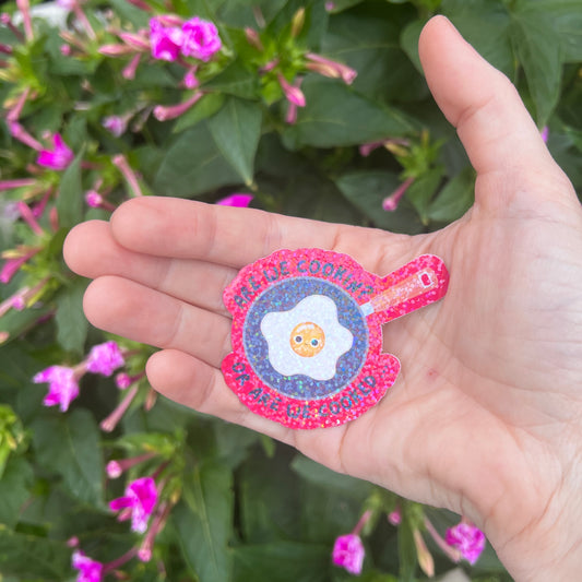 Holographic vinyl sticker with a wide-eyed egg in a frying pan and the phrase “Are We Cooking or Are We Cooked?” Funny kitchen-themed design.