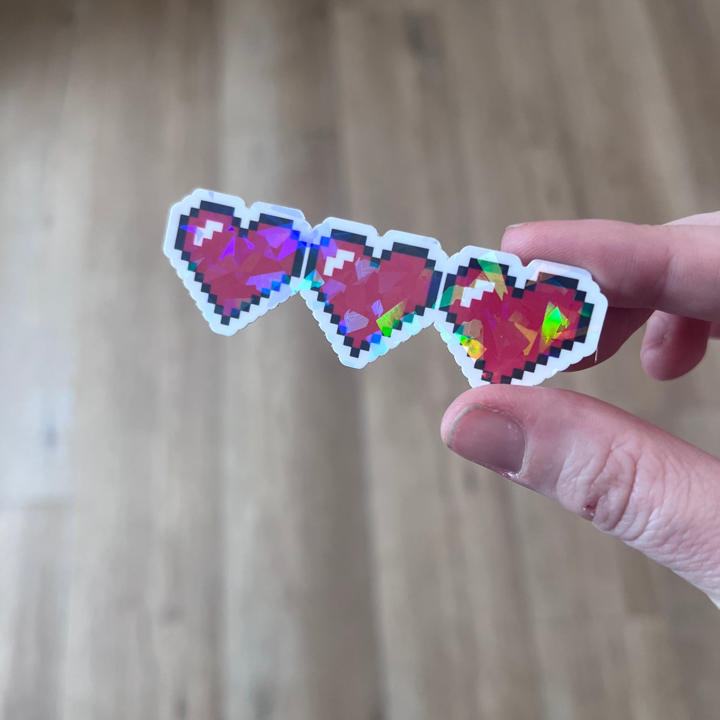 Holographic gamer heart sticker featuring 3 red pixel hearts in a heart container design. Perfect for laptops, water bottles, and game-themed journals.
