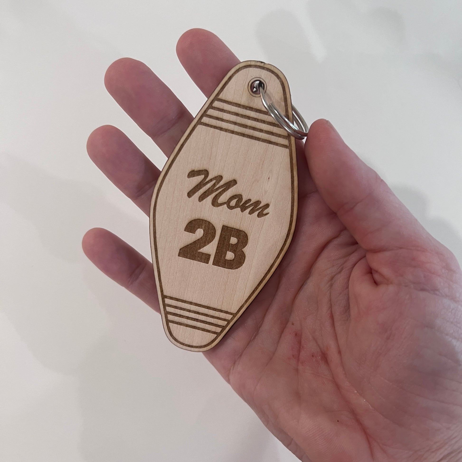 Laser engraved wooden motel keychain with “Mom 2B” design. A cute keepsake or gift for baby showers, pregnancy announcements, or expecting moms.