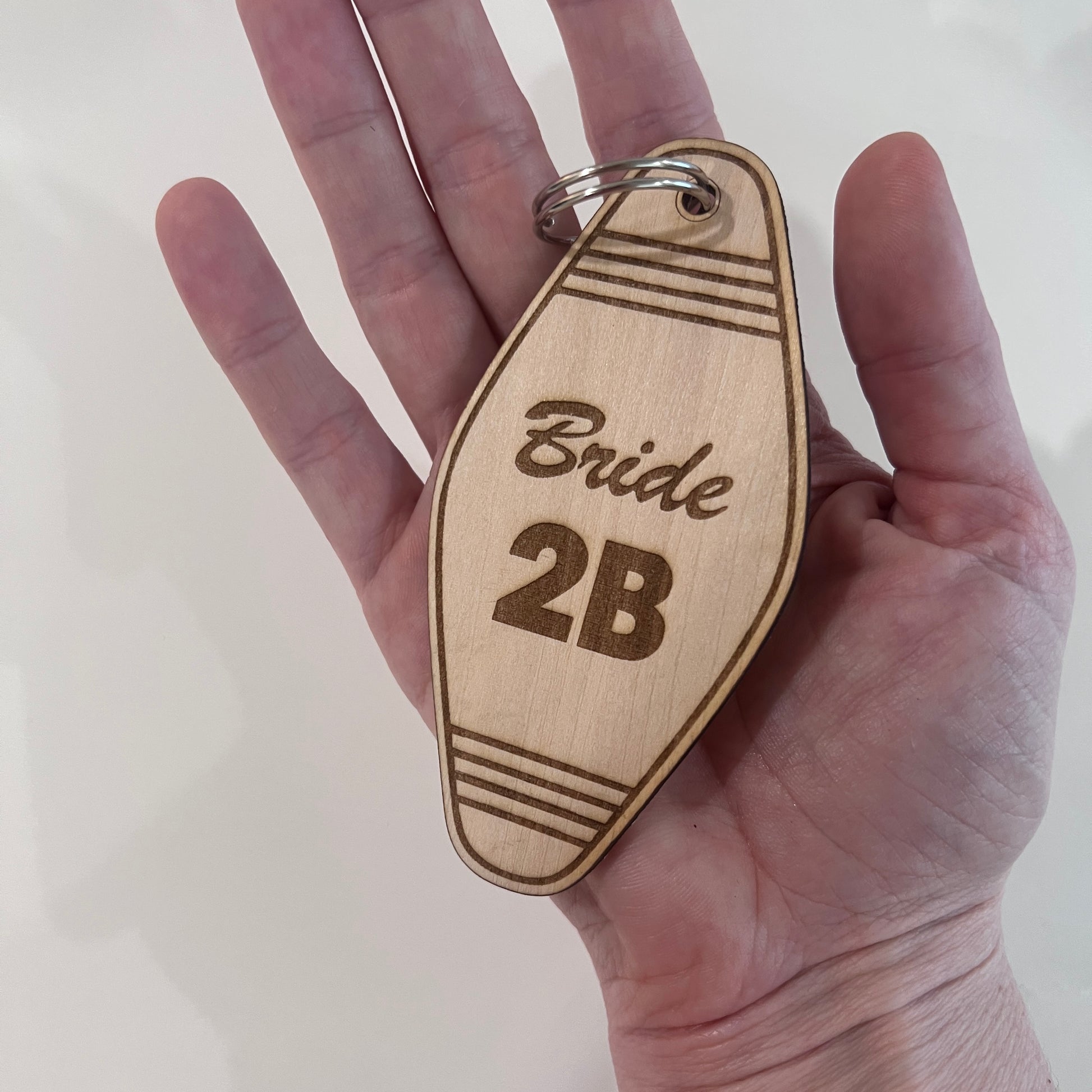 Wooden keychain with 'Bride 2B' text held in a hand against a white background