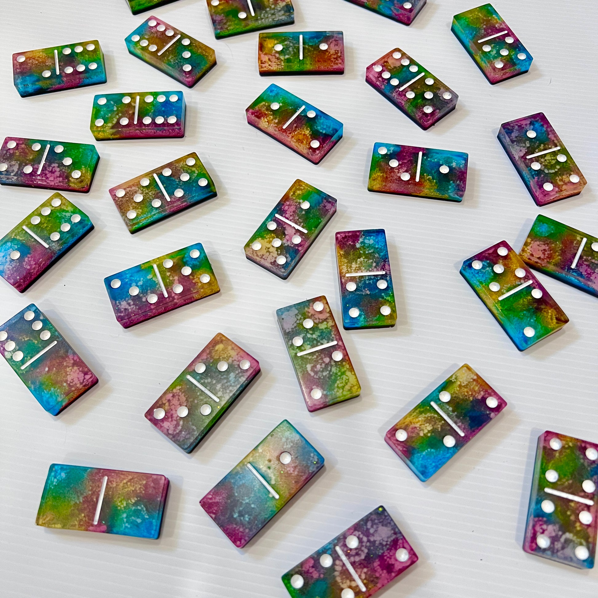 Handmade resin domino set with vibrant rainbow petri designs and holographic glitter backing. Bold black base adds contrast for striking game night flair.
