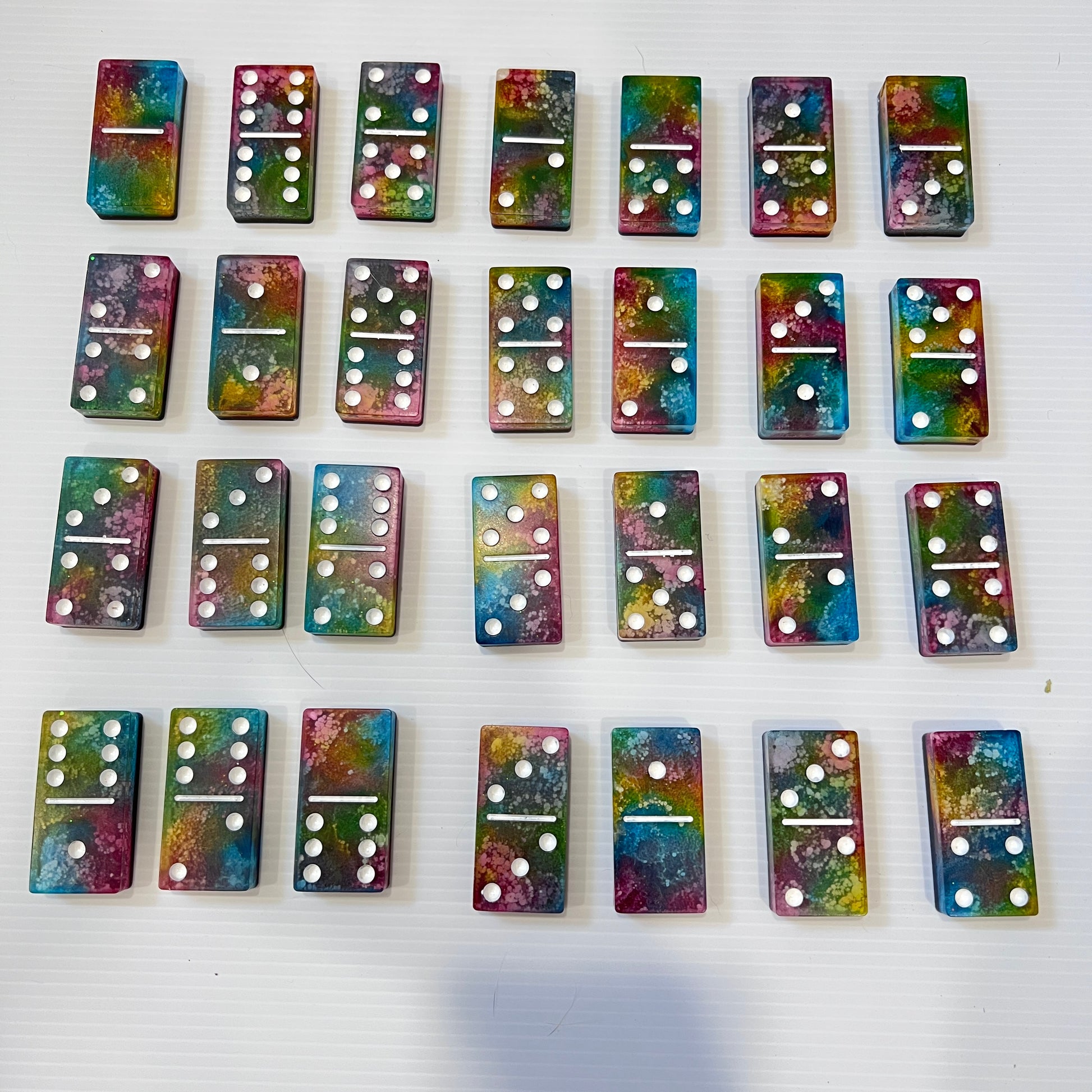 Handmade resin domino set with vibrant rainbow petri designs and holographic glitter backing. Bold black base adds contrast for striking game night flair.