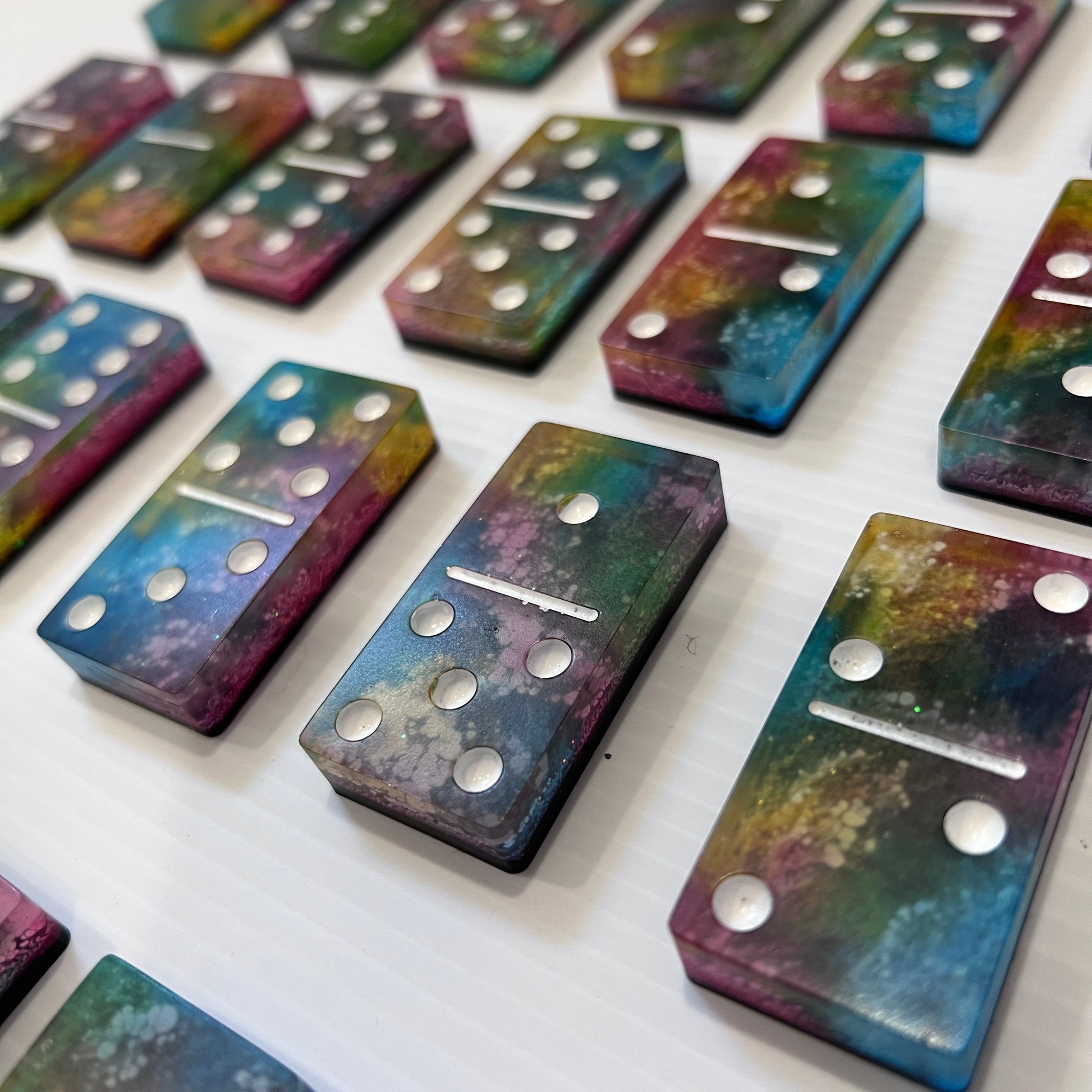 Handmade resin domino set with vibrant rainbow petri designs and holographic glitter backing. Bold black base adds contrast for striking game night flair.