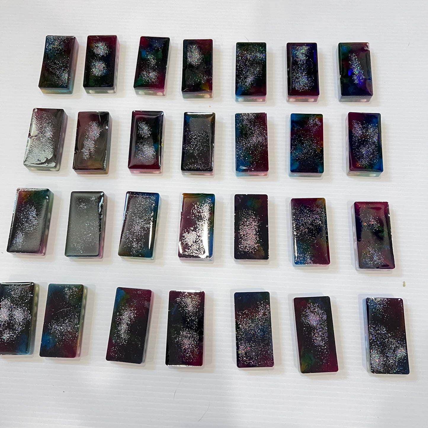 Handmade resin domino set with vibrant rainbow petri designs and holographic glitter backing. Bold black base adds contrast for striking game night flair.