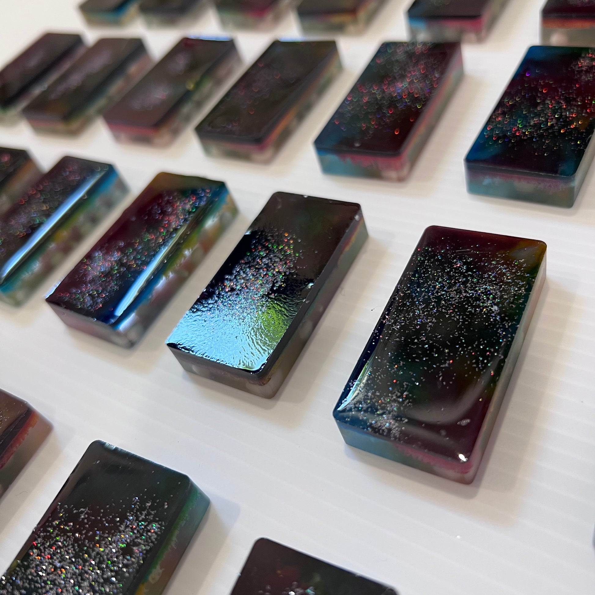 Handmade resin domino set with vibrant rainbow petri designs and holographic glitter backing. Bold black base adds contrast for striking game night flair.