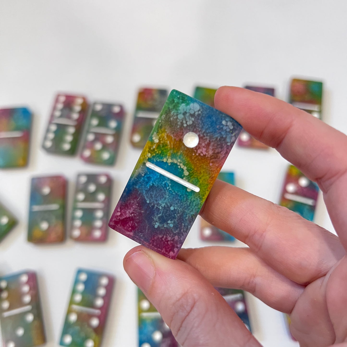 Handmade resin domino set with vibrant rainbow petri designs and holographic glitter backing. Bold black base adds contrast for striking game night flair.