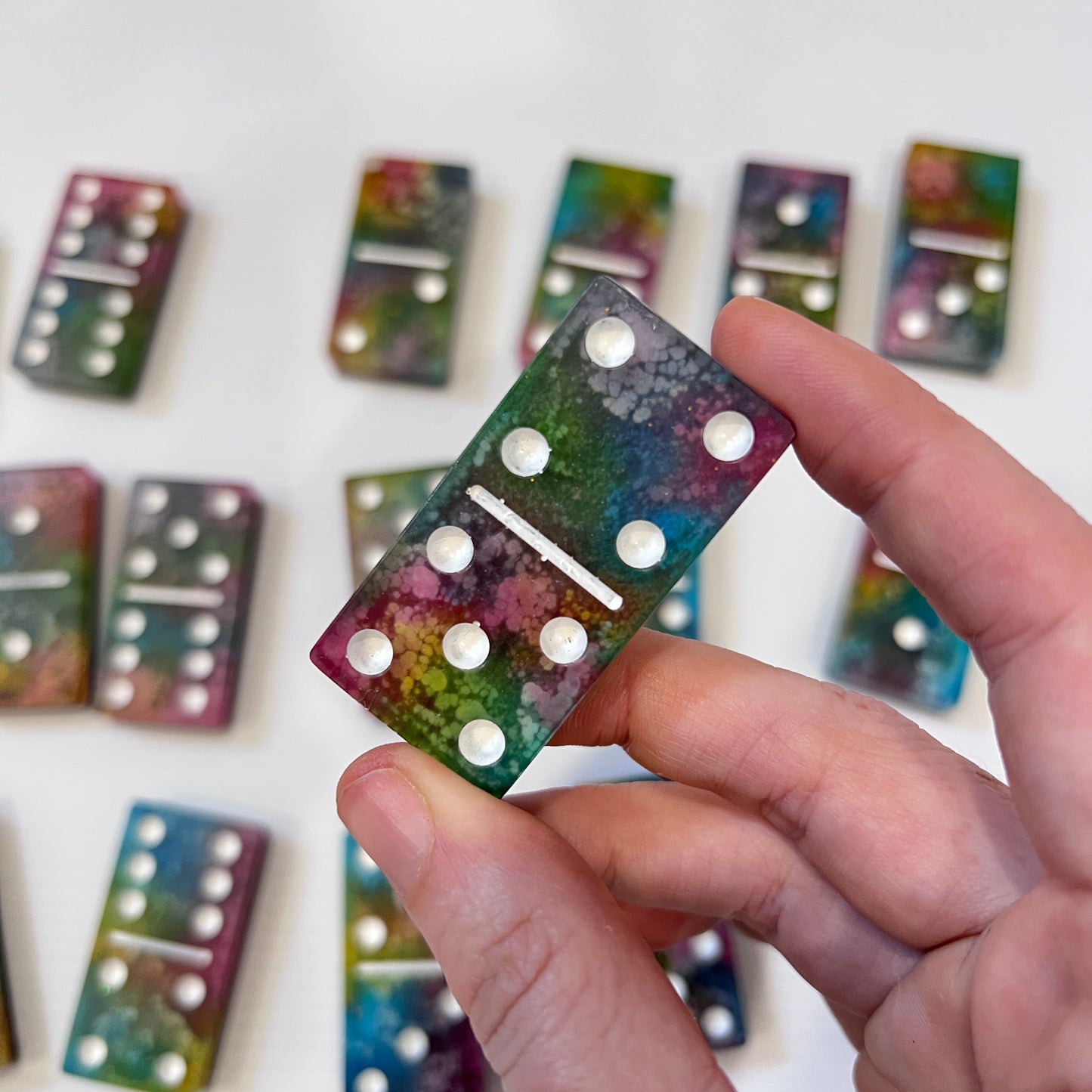 Handmade resin domino set with vibrant rainbow petri designs and holographic glitter backing. Bold black base adds contrast for striking game night flair.