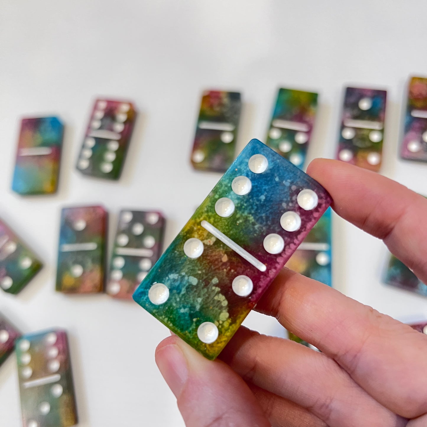 Handmade resin domino set with vibrant rainbow petri designs and holographic glitter backing. Bold black base adds contrast for striking game night flair.