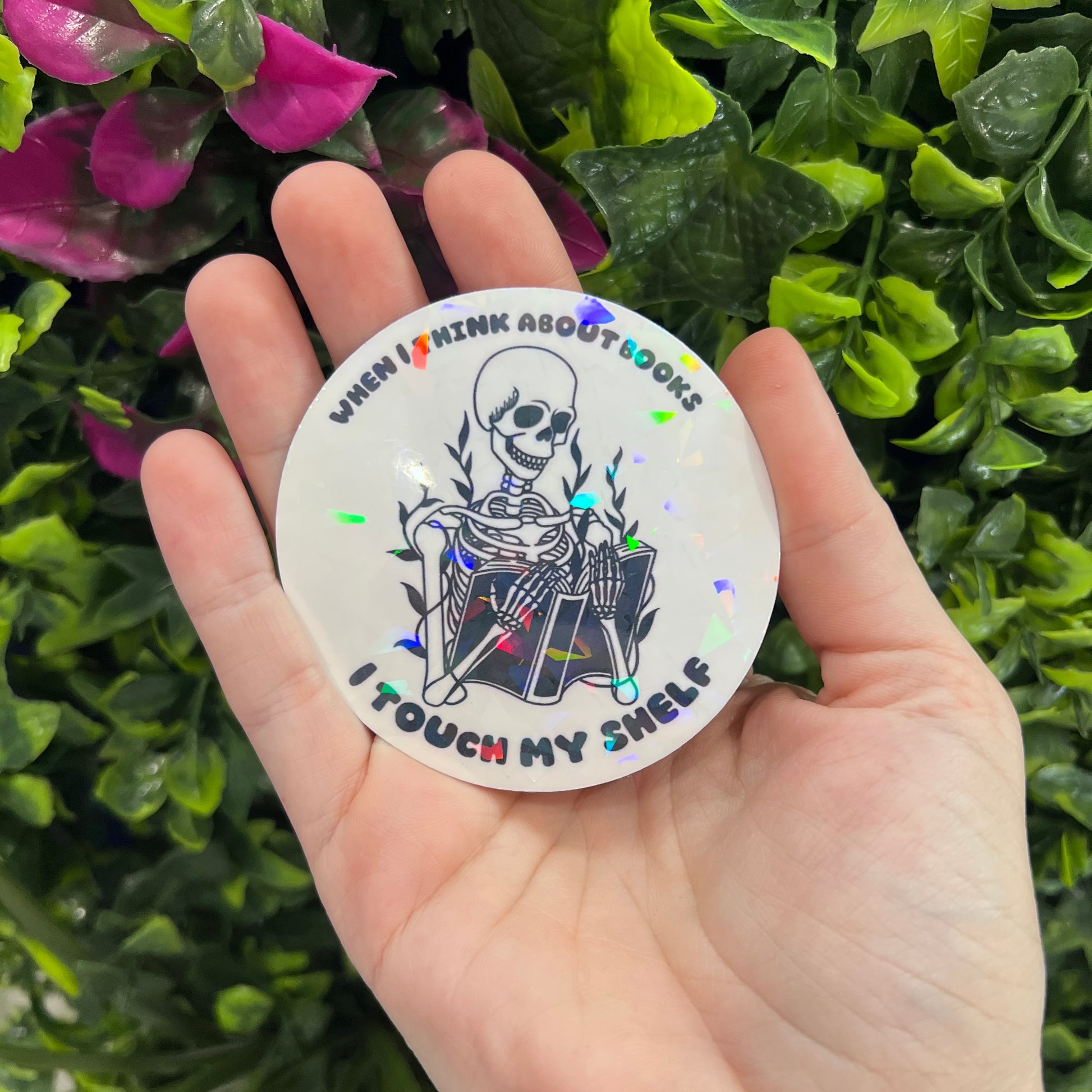 Holographic vinyl sticker with a skeleton reading a book and the phrase "When I think about books I touch my shelf." Perfect for readers and book lovers.