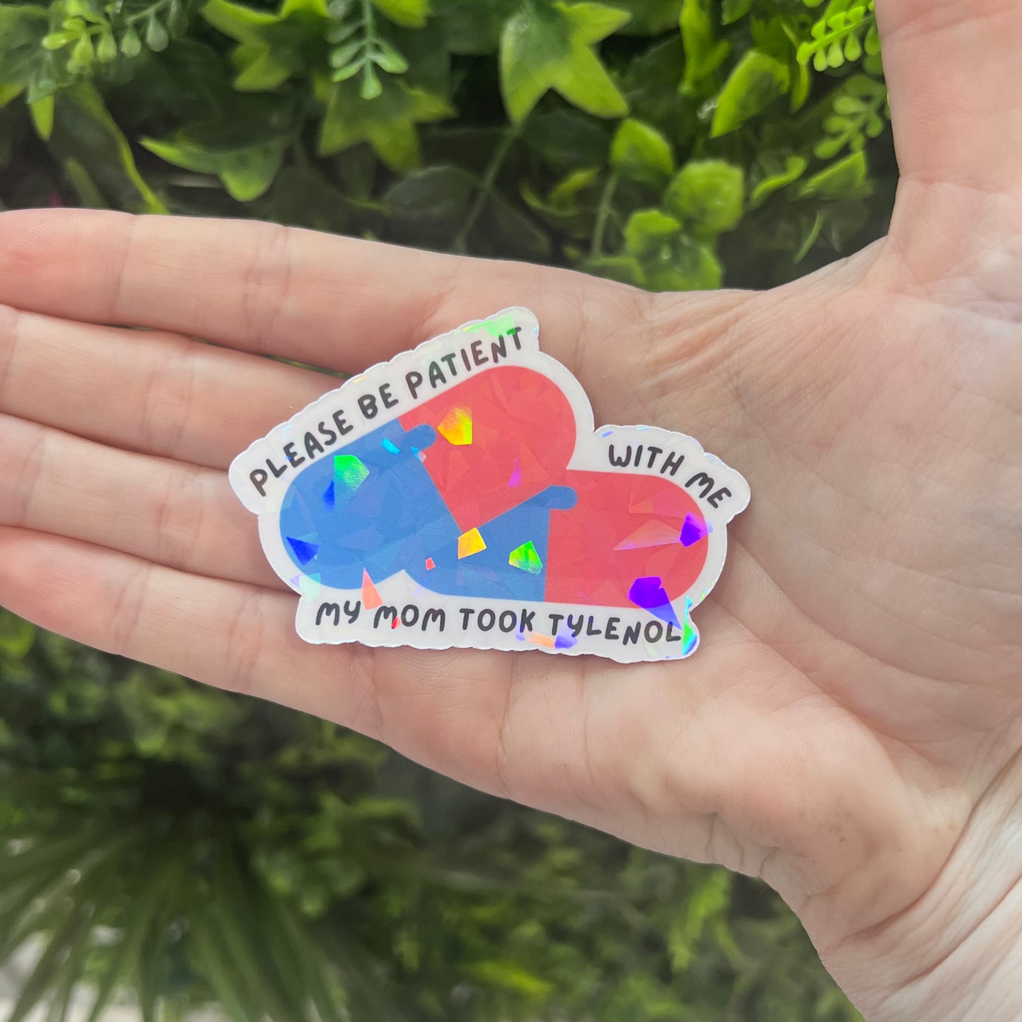 Holographic sticker featuring two pills and the phrase “Please be patient with me my mom took Tylenol.” Funny, shiny mental health vinyl decal for laptops, water bottles, and more.