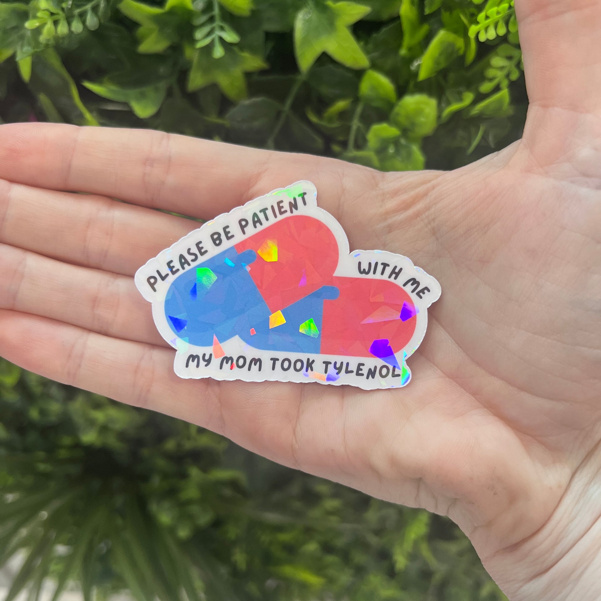 Holographic sticker featuring two pills and the phrase “Please be patient with me my mom took Tylenol.” Funny, shiny mental health vinyl decal for laptops, water bottles, and more.