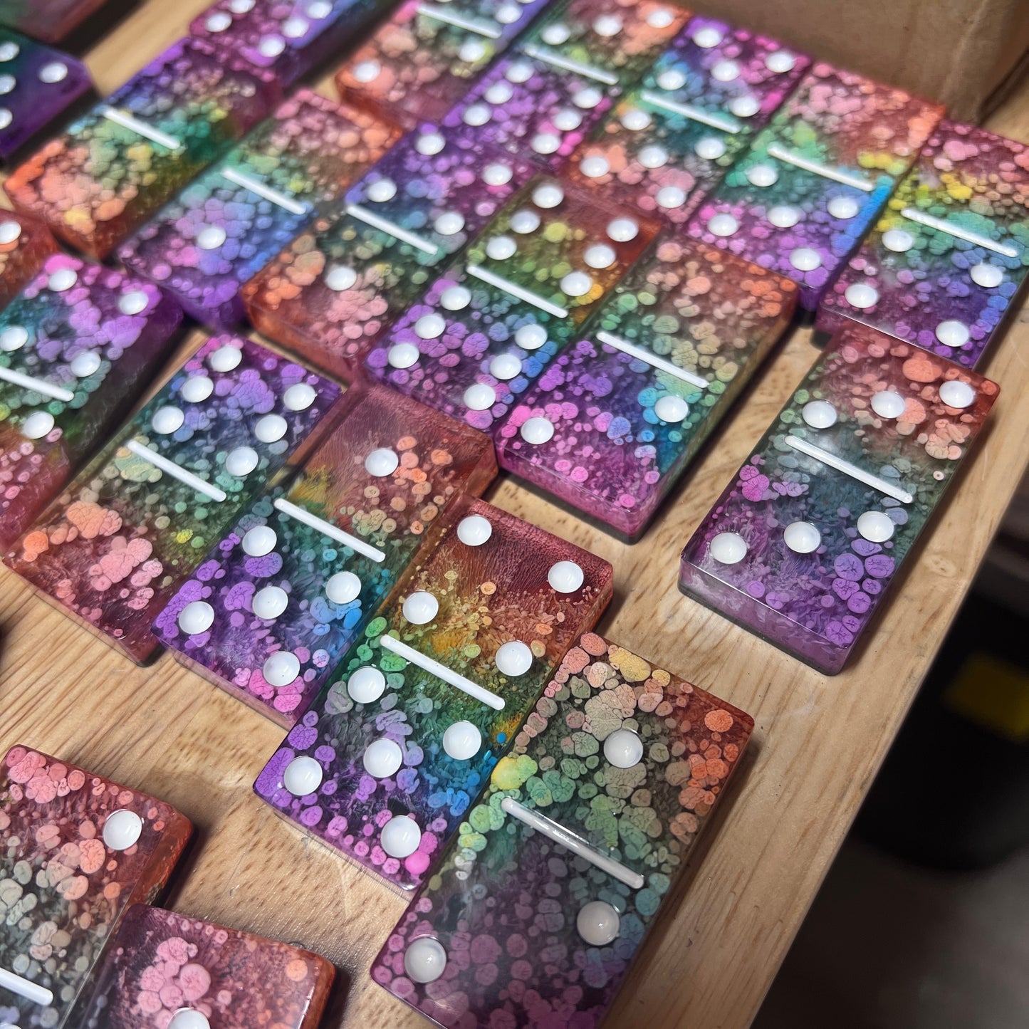 Handmade resin domino set with vibrant rainbow petri designs and holographic glitter backing. Bold black base adds contrast for striking game night flair.