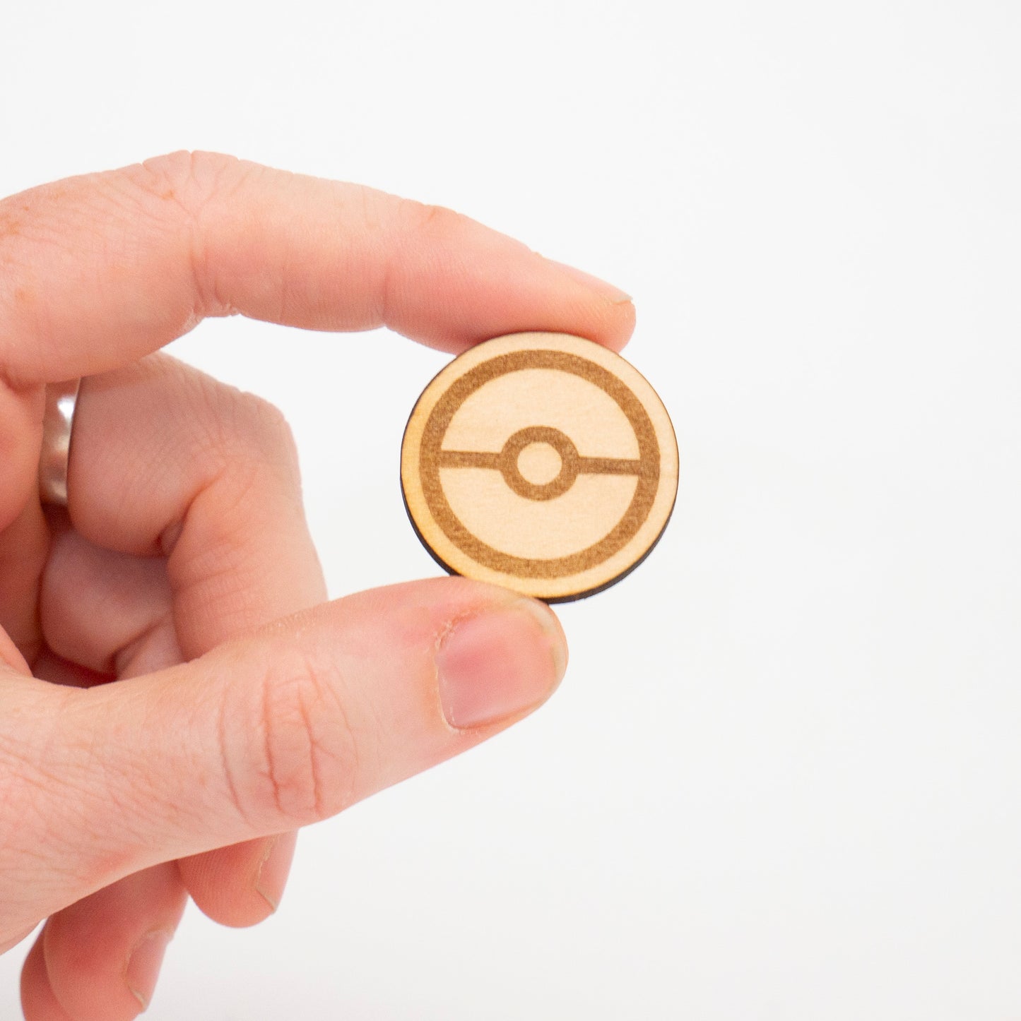 Hand holding a wooden Poké Ball pin against a white background