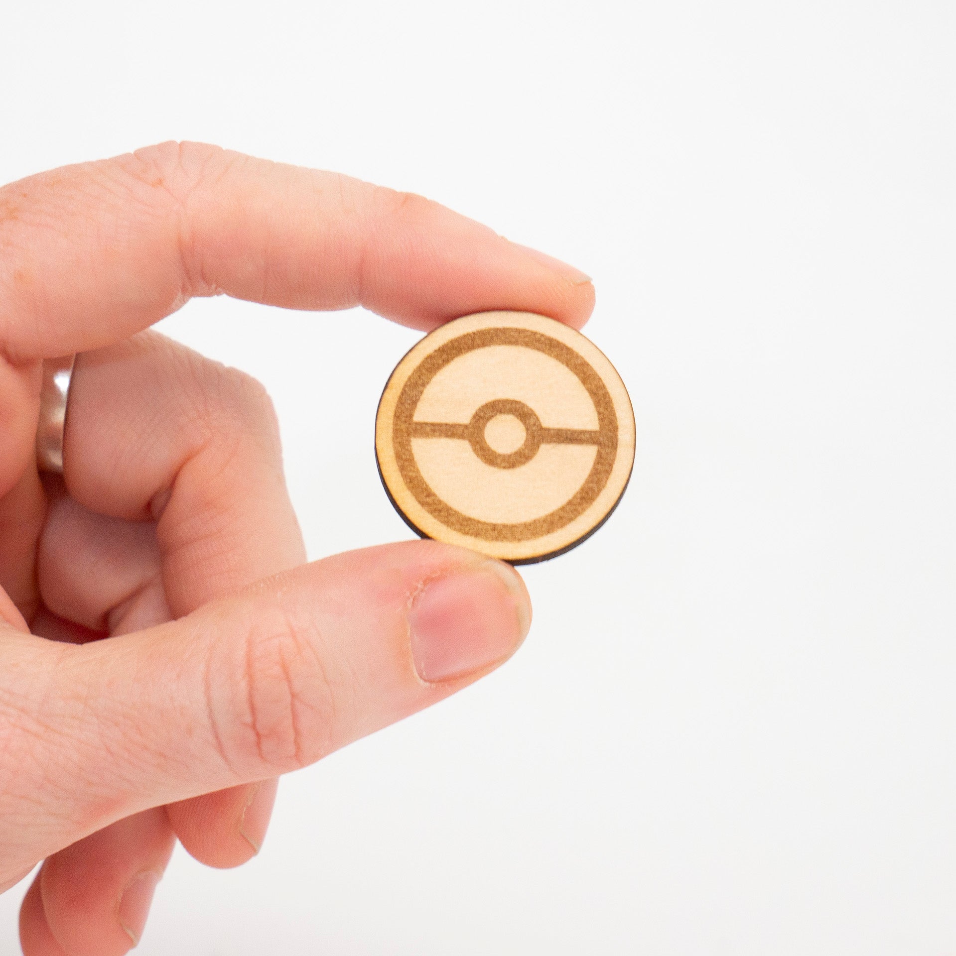Hand holding a wooden Poké Ball pin against a white background