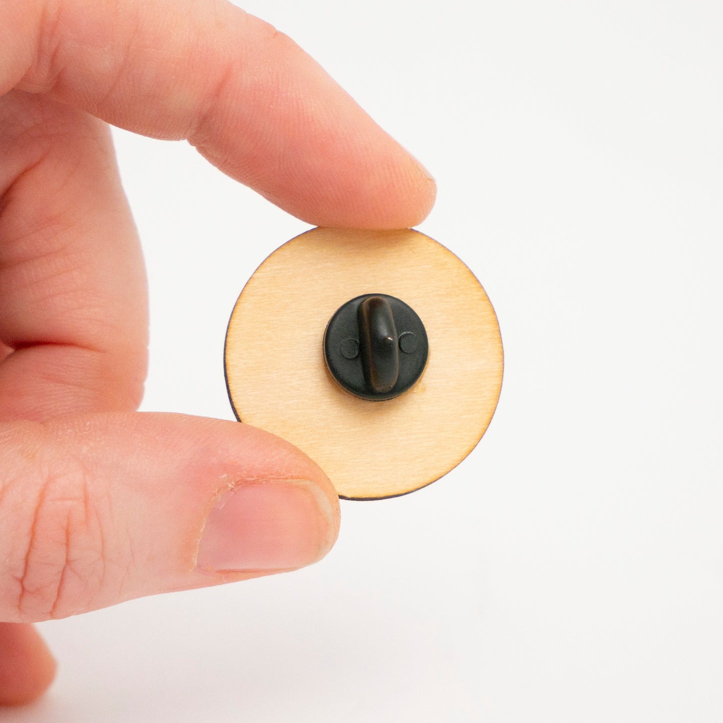 Hand holding a wooden Poké Ball pin against a white background