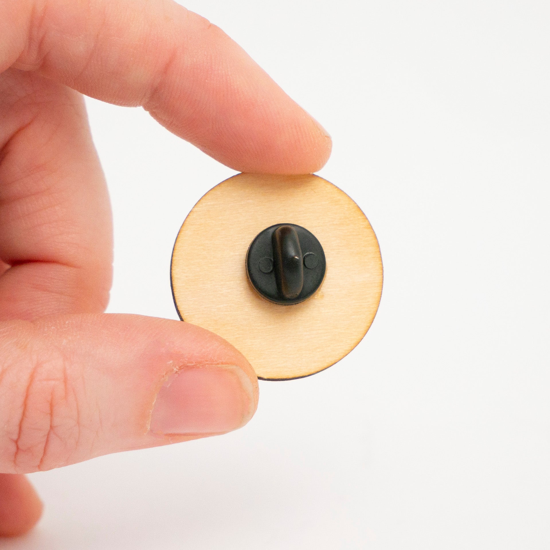 Hand holding a wooden Poké Ball pin against a white background