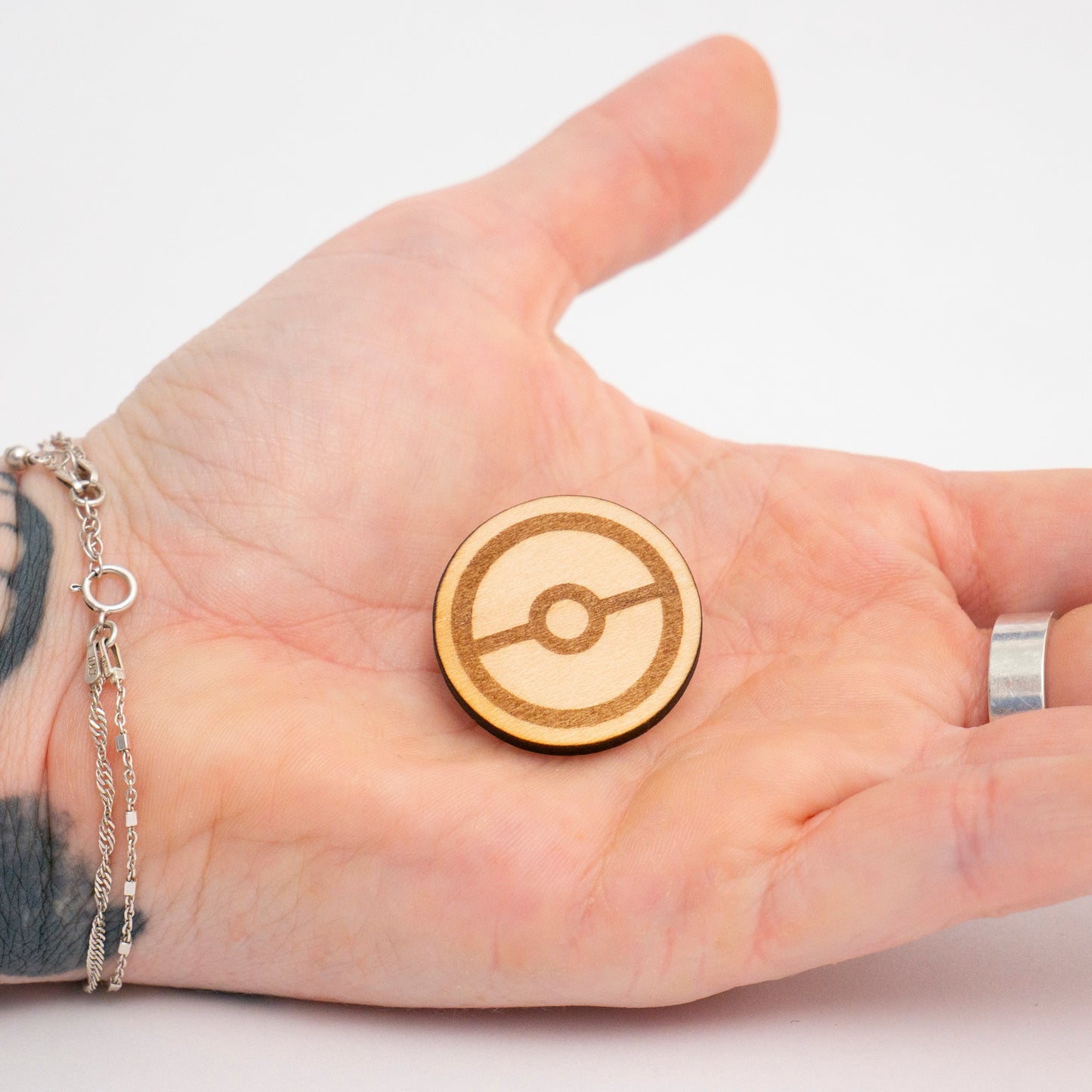 Hand holding a wooden Poké Ball pin against a white background