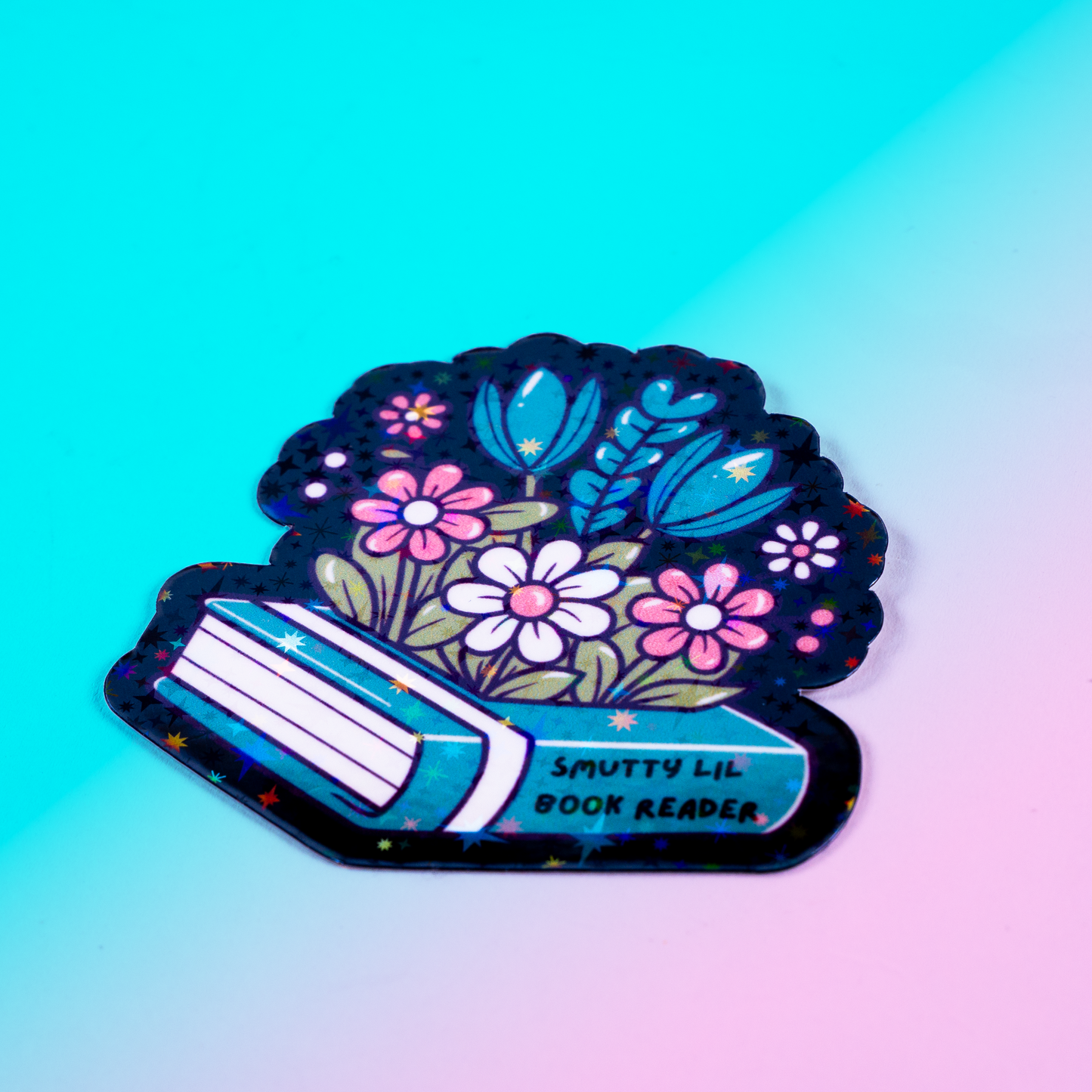 Holographic vinyl sticker featuring flowers growing from a romance book labeled "Smutty Lil Book Reader." Perfect for book lovers, Kindle cases, and bookish decor.