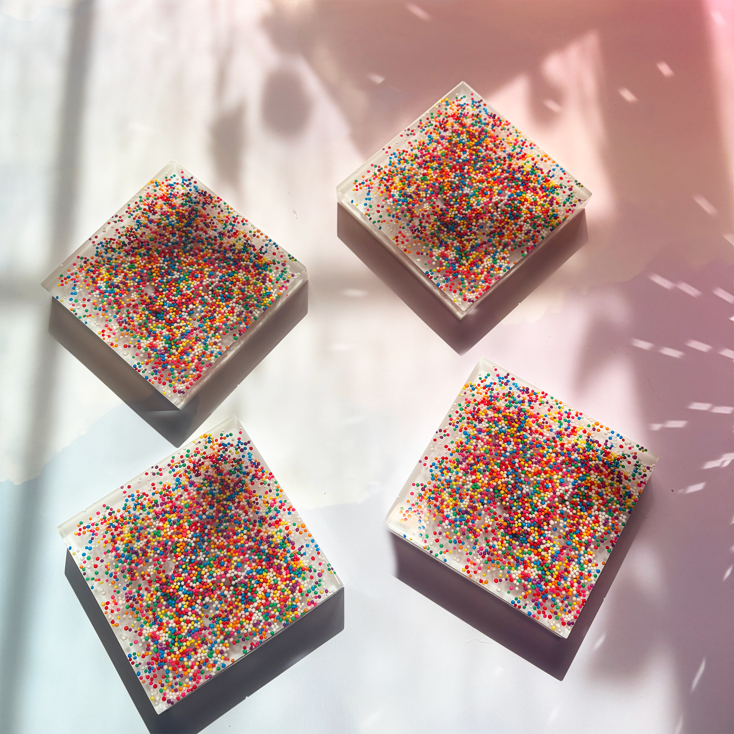 Resin coaster inlaid with rainbow sprinkles and white backing.