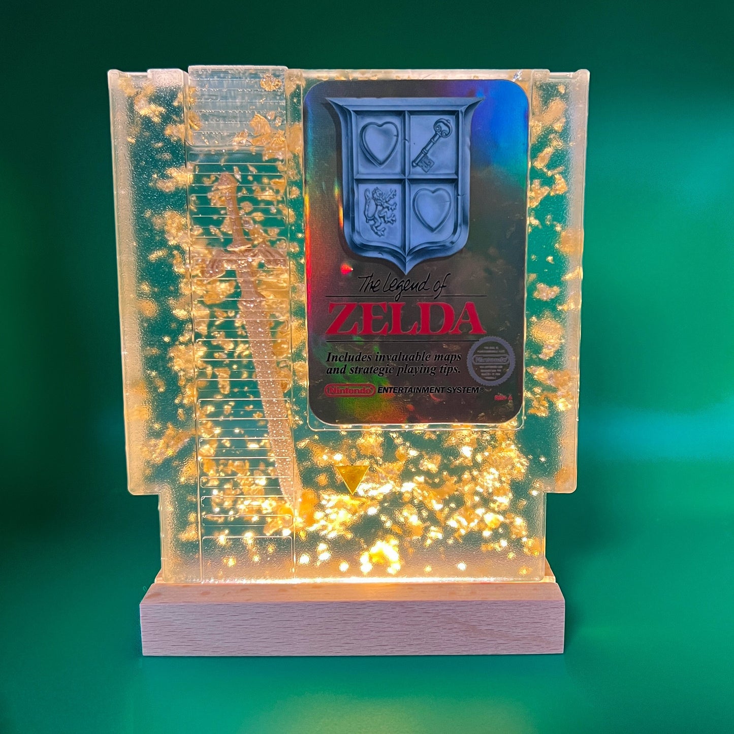 Legend of Zelda resin art featuring a retro NES cartridge with a gold sword design and gold flakes embedded. This handmade display is perfect for gamers and video game collectors, offering a unique décor piece for any gaming setup or retro collection