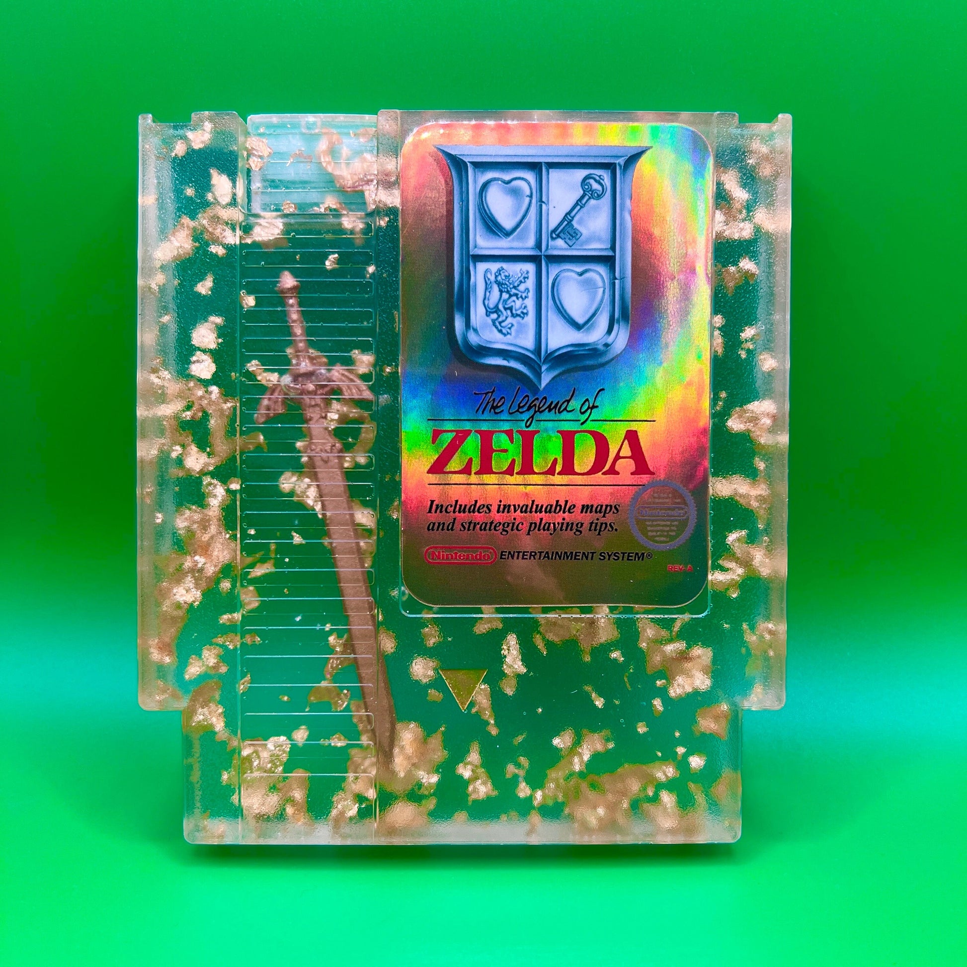 Legend of Zelda resin art featuring a retro NES cartridge with a gold sword design and gold flakes embedded. This handmade display is perfect for gamers and video game collectors, offering a unique décor piece for any gaming setup or retro collection