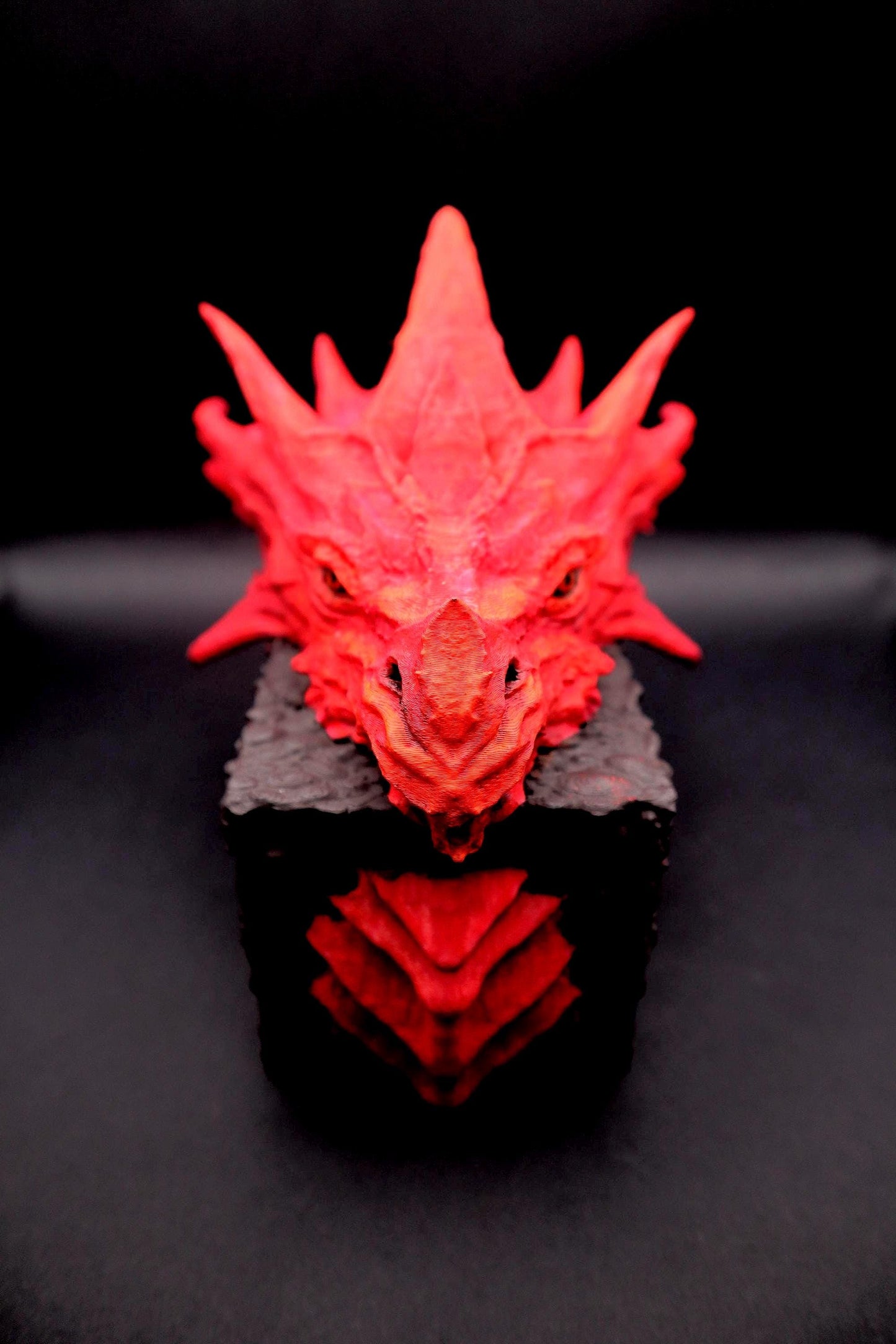 A red dragon head sculpture with a textured surface. The sculpture is on a black base. Red dragon-themed dice case with resin dice set, perfect for DnD and RPG players. Stylish fantasy dice holder and storage box for tabletop gaming sessions.