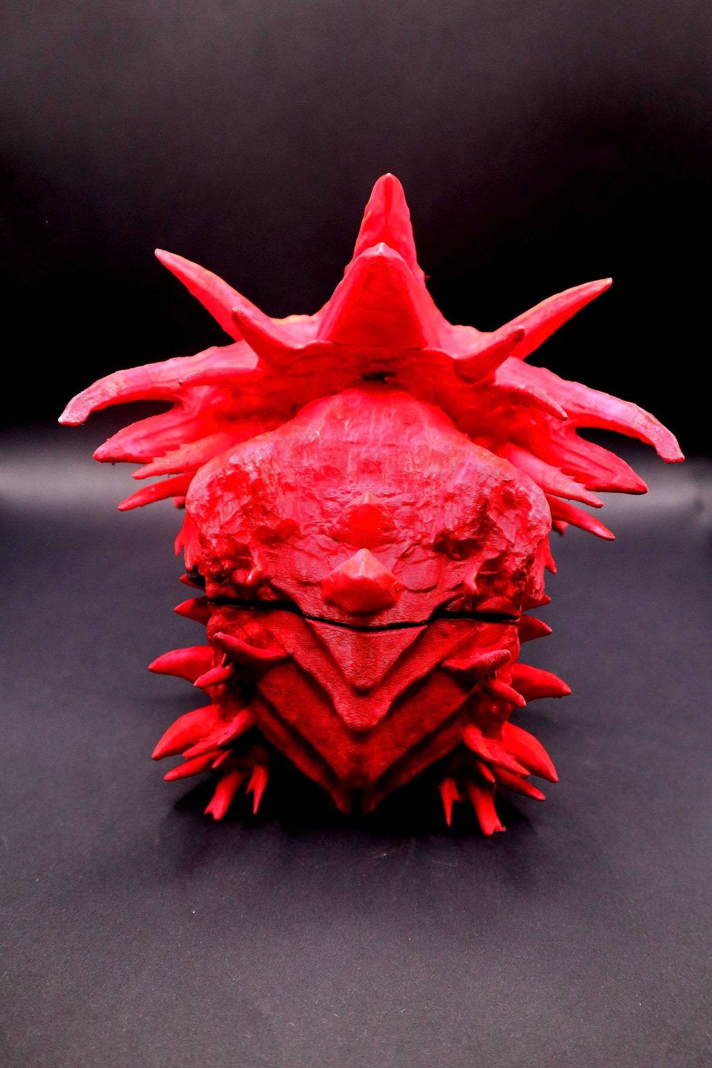 A red, spiky, handpainted 3D printed sculpture of a creature with a crown-like head and a textured surface. Red dragon-themed dice case with resin dice set, perfect for DnD and RPG players. Stylish fantasy dice holder and storage box for tabletop gaming sessions.
