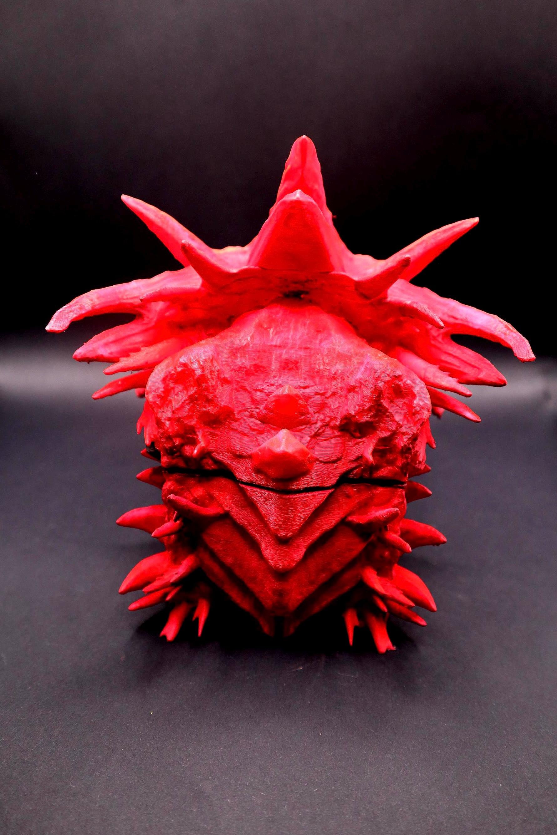 A red, spiky, handpainted 3D printed sculpture of a creature with a crown-like head and a textured surface. Red dragon-themed dice case with resin dice set, perfect for DnD and RPG players. Stylish fantasy dice holder and storage box for tabletop gaming sessions.
