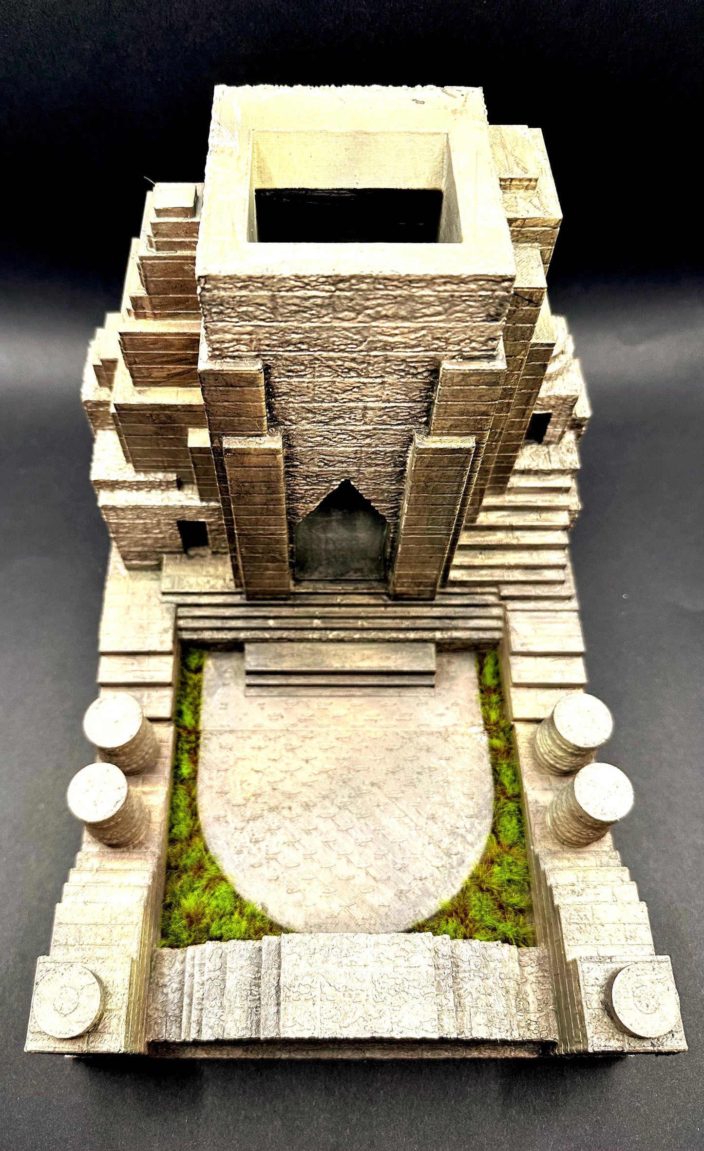A handpainted explorer temple dice tower with a tan and brown color scheme. The tower features a detailed, textured design of a delapidated temple Laura Croft might explore. The tower has miniature green grass around the tray that catches the dice. Perfect for dice goblins and ttrpg lovers alike. The perfect item for your next dungeons and dragons campaign.