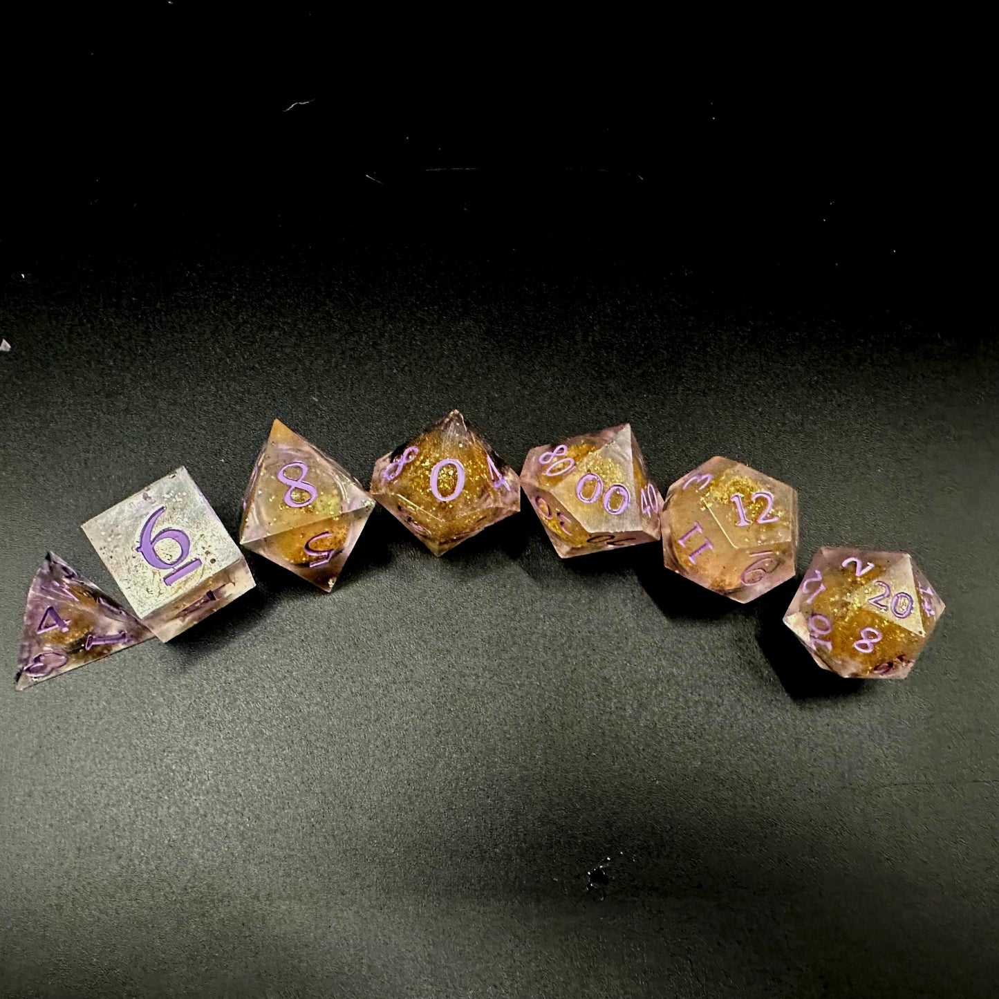 Light purple, pink, and gold glitter liquid core dice set shimmering with swirling metallic sparkle. Handcrafted polyhedral resin dice filled with floating glitter and vibrant liquid core for mesmerizing movement. Perfect for Dungeons & Dragons, tabletop RPGs, and dice collectors. Elegant pastel tones with gold accents add a magical, fantasy-inspired aesthetic for gaming sessions or gift giving.