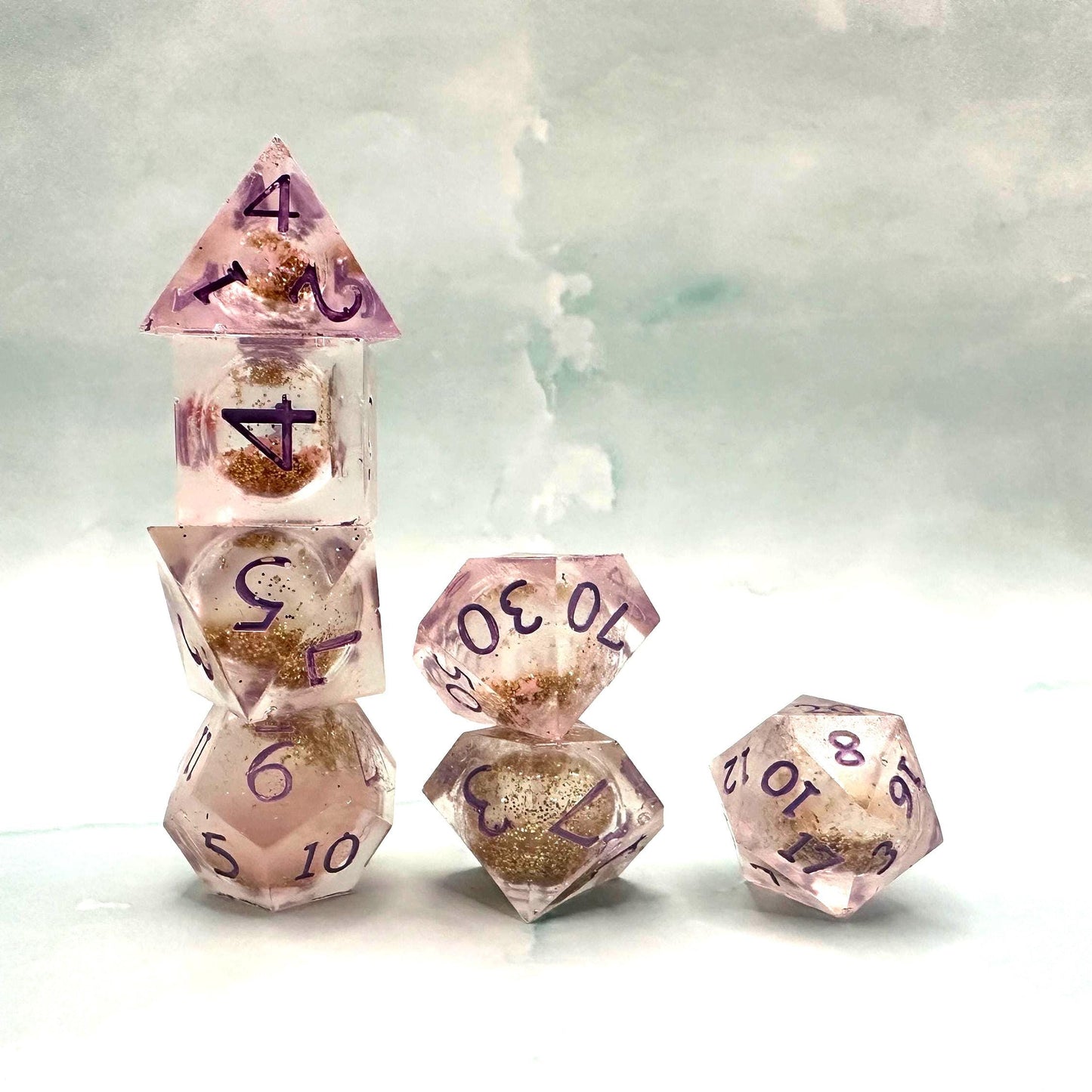 Light purple, pink, and gold glitter liquid core dice set shimmering with swirling metallic sparkle. Handcrafted polyhedral resin dice filled with floating glitter and vibrant liquid core for mesmerizing movement. Perfect for Dungeons & Dragons, tabletop RPGs, and dice collectors. Elegant pastel tones with gold accents add a magical, fantasy-inspired aesthetic for gaming sessions or gift giving.