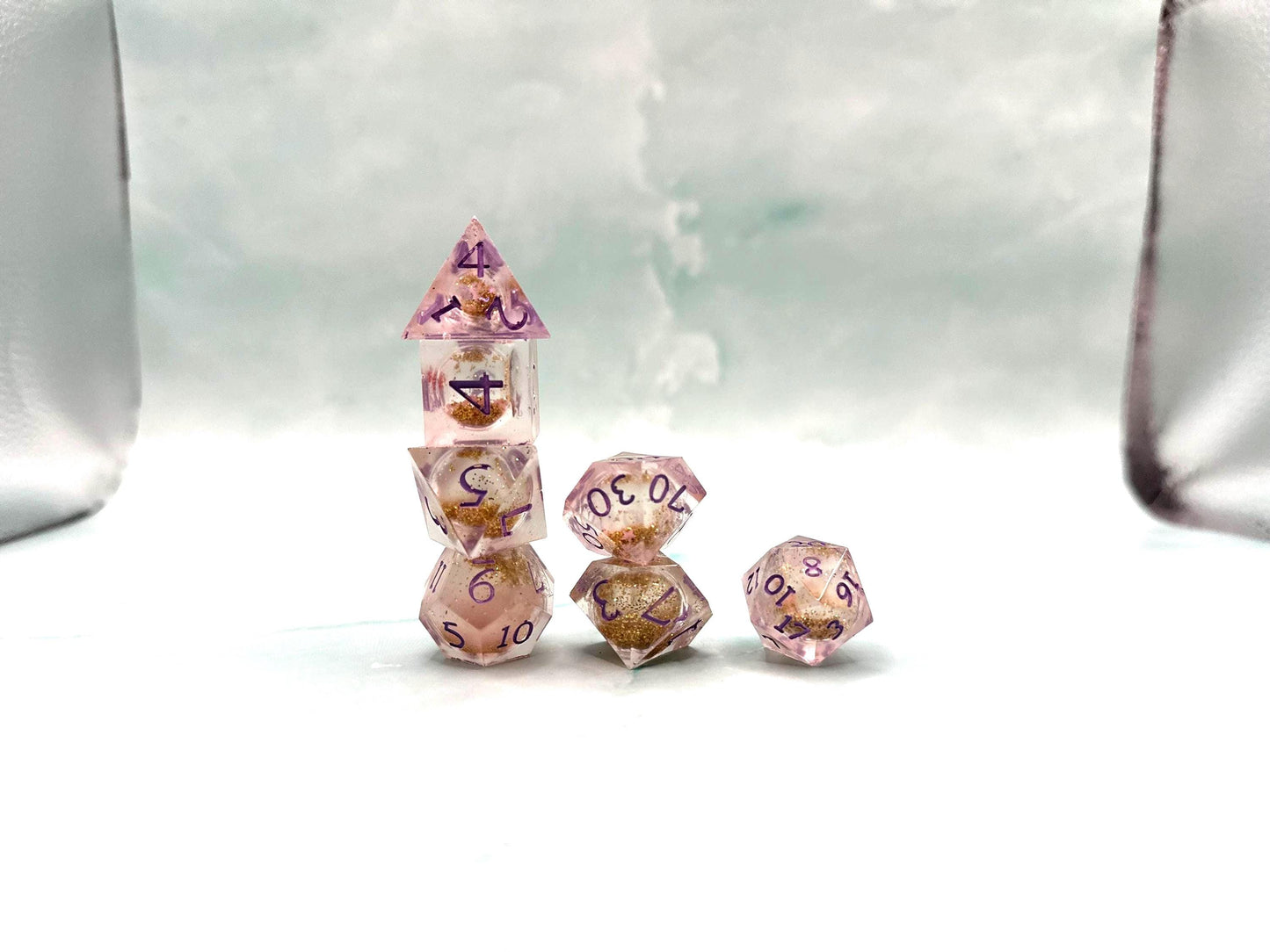 Light purple, pink, and gold glitter liquid core dice set shimmering with swirling metallic sparkle. Handcrafted polyhedral resin dice filled with floating glitter and vibrant liquid core for mesmerizing movement. Perfect for Dungeons & Dragons, tabletop RPGs, and dice collectors. Elegant pastel tones with gold accents add a magical, fantasy-inspired aesthetic for gaming sessions or gift giving.