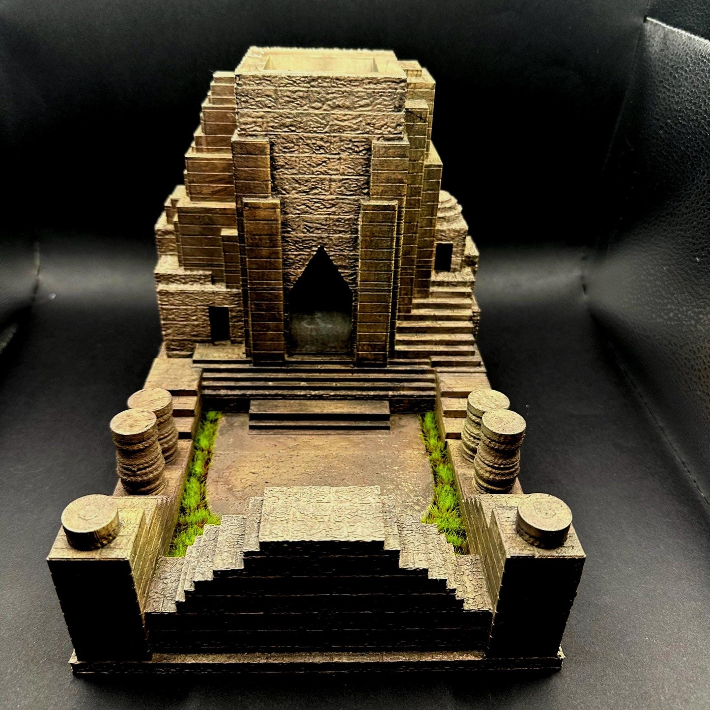 A handpainted explorer temple dice tower with a tan and brown color scheme. The tower features a detailed, textured design of a delapidated temple Laura Croft might explore. The tower has miniature green grass around the tray that catches the dice. Perfect for dice goblins and ttrpg lovers alike. The perfect item for your next dungeons and dragons campaign.