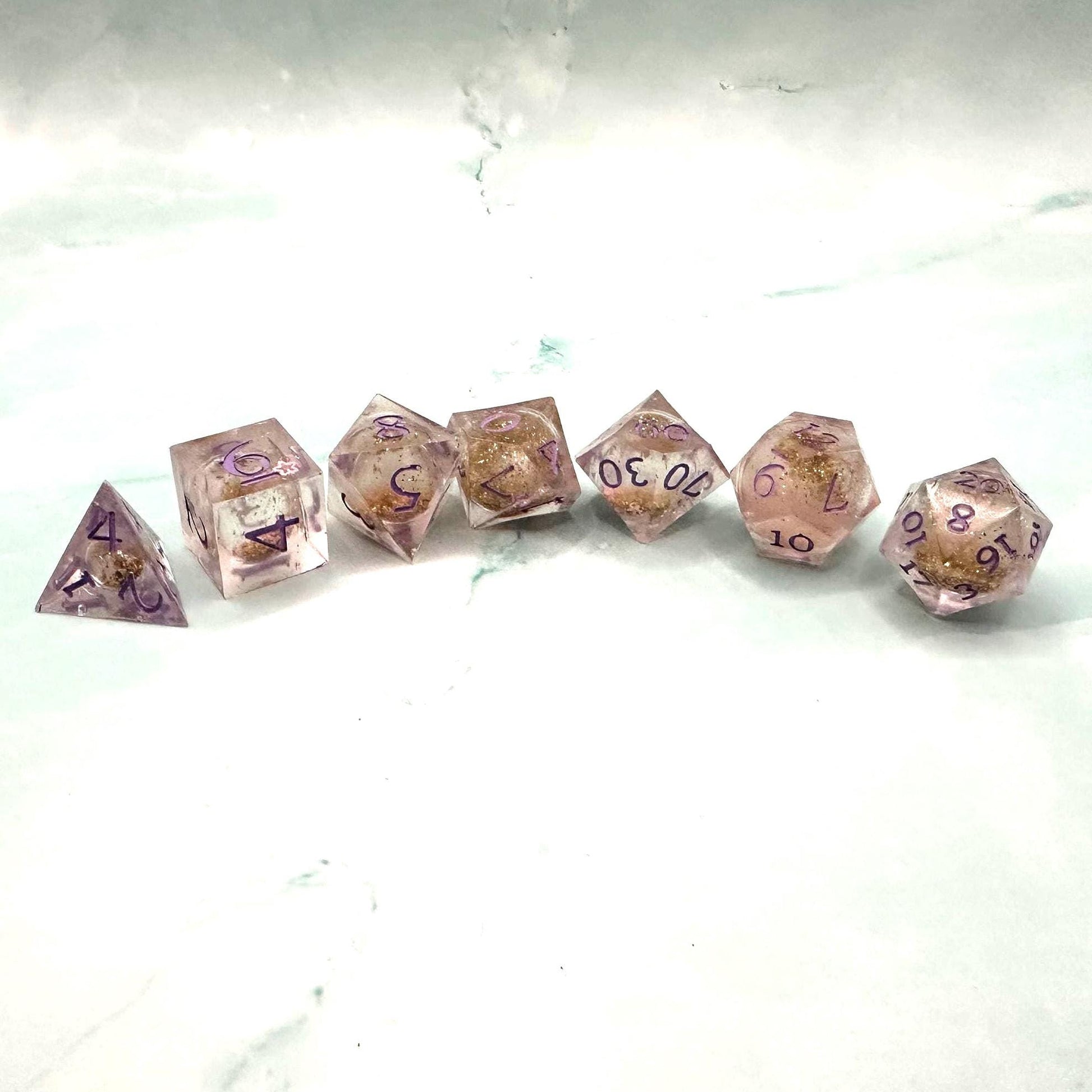 Light purple, pink, and gold glitter liquid core dice set shimmering with swirling metallic sparkle. Handcrafted polyhedral resin dice filled with floating glitter and vibrant liquid core for mesmerizing movement. Perfect for Dungeons & Dragons, tabletop RPGs, and dice collectors. Elegant pastel tones with gold accents add a magical, fantasy-inspired aesthetic for gaming sessions or gift giving.