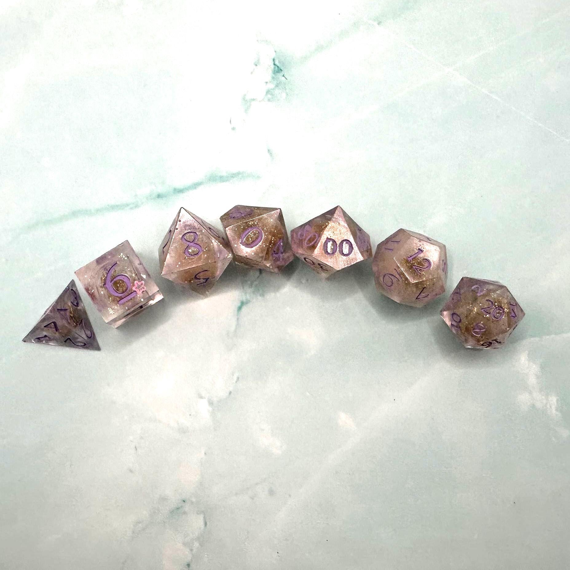 Light purple, pink, and gold glitter liquid core dice set shimmering with swirling metallic sparkle. Handcrafted polyhedral resin dice filled with floating glitter and vibrant liquid core for mesmerizing movement. Perfect for Dungeons & Dragons, tabletop RPGs, and dice collectors. Elegant pastel tones with gold accents add a magical, fantasy-inspired aesthetic for gaming sessions or gift giving.