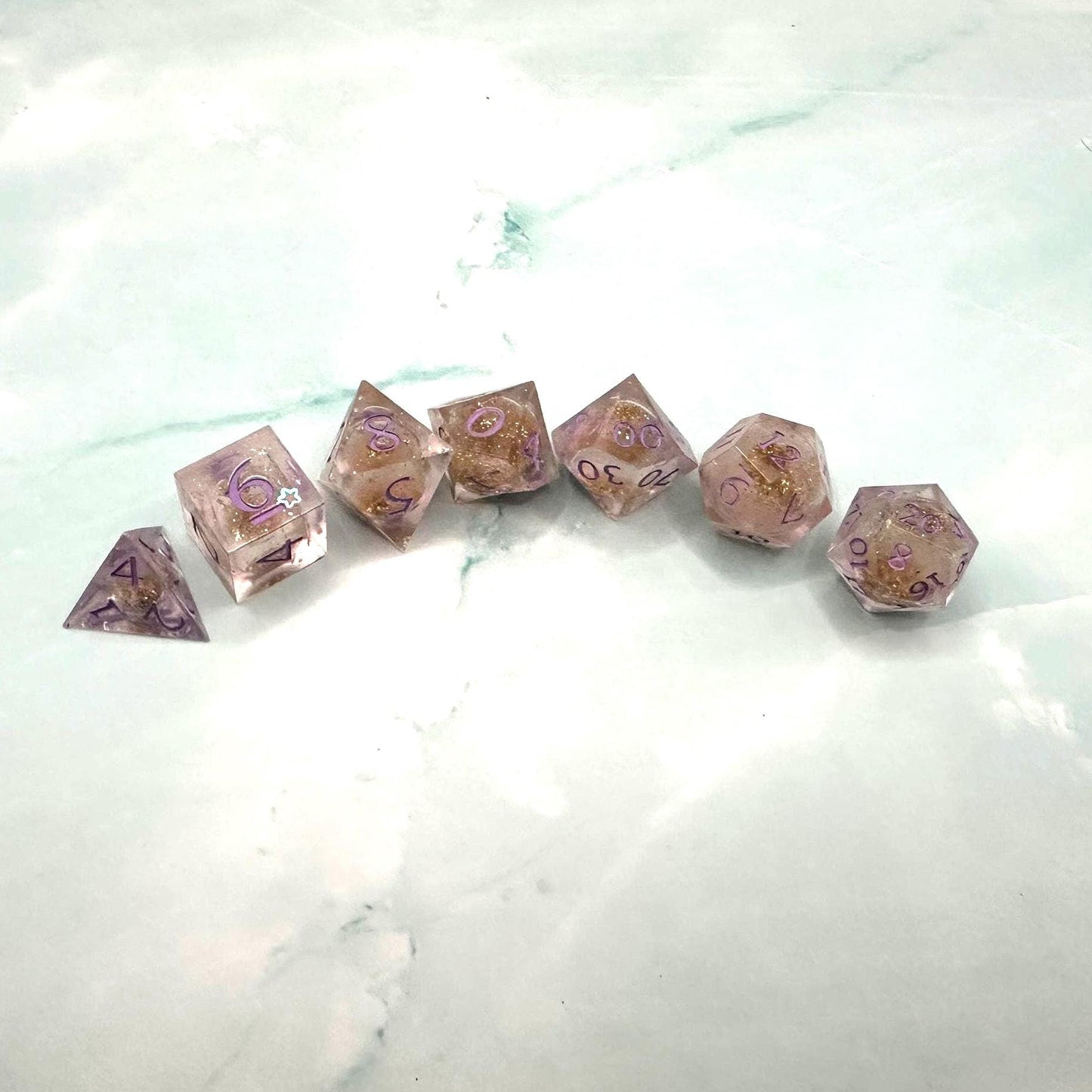 Light purple, pink, and gold glitter liquid core dice set shimmering with swirling metallic sparkle. Handcrafted polyhedral resin dice filled with floating glitter and vibrant liquid core for mesmerizing movement. Perfect for Dungeons & Dragons, tabletop RPGs, and dice collectors. Elegant pastel tones with gold accents add a magical, fantasy-inspired aesthetic for gaming sessions or gift giving.