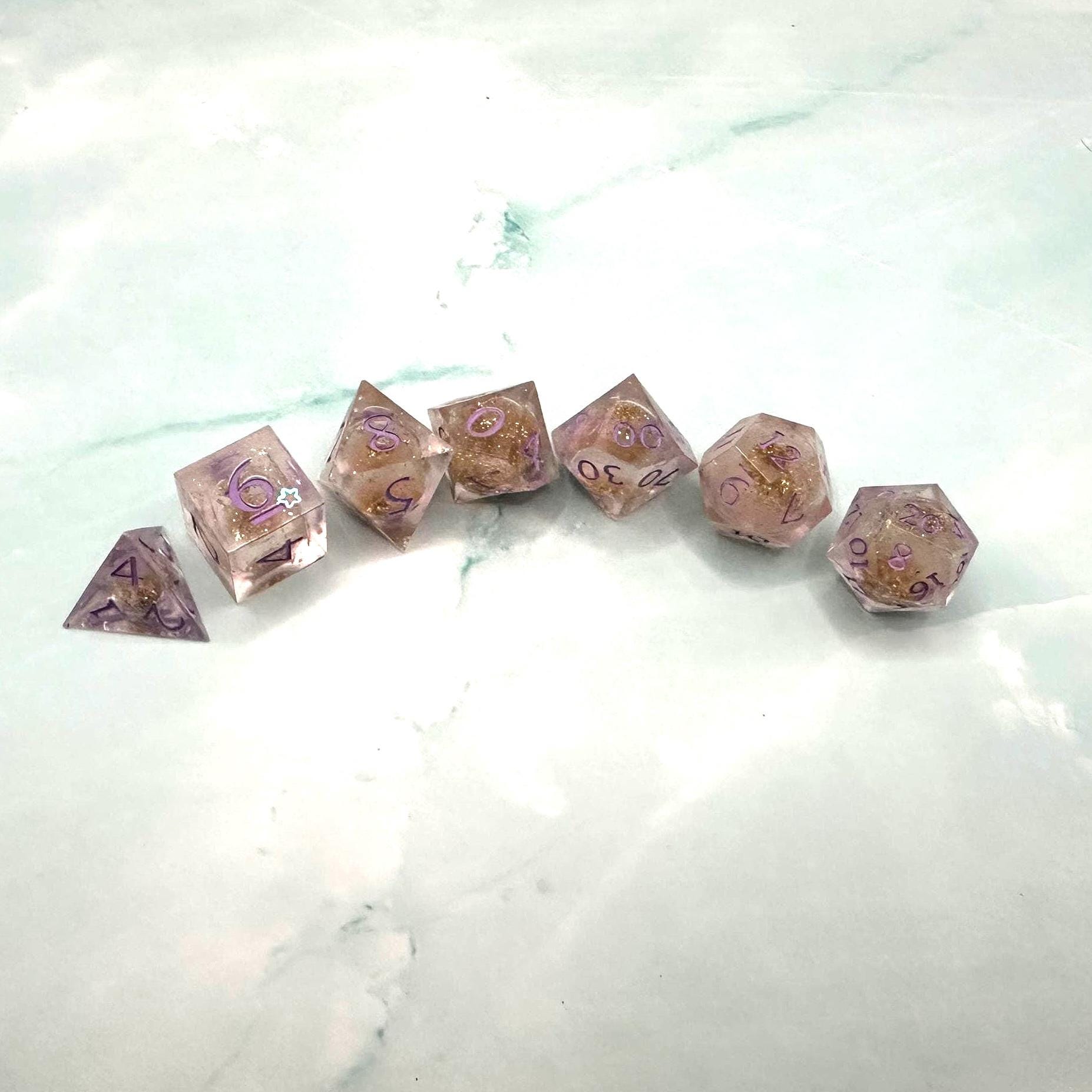 Light purple, pink, and gold glitter liquid core dice set shimmering with swirling metallic sparkle. Handcrafted polyhedral resin dice filled with floating glitter and vibrant liquid core for mesmerizing movement. Perfect for Dungeons & Dragons, tabletop RPGs, and dice collectors. Elegant pastel tones with gold accents add a magical, fantasy-inspired aesthetic for gaming sessions or gift giving.