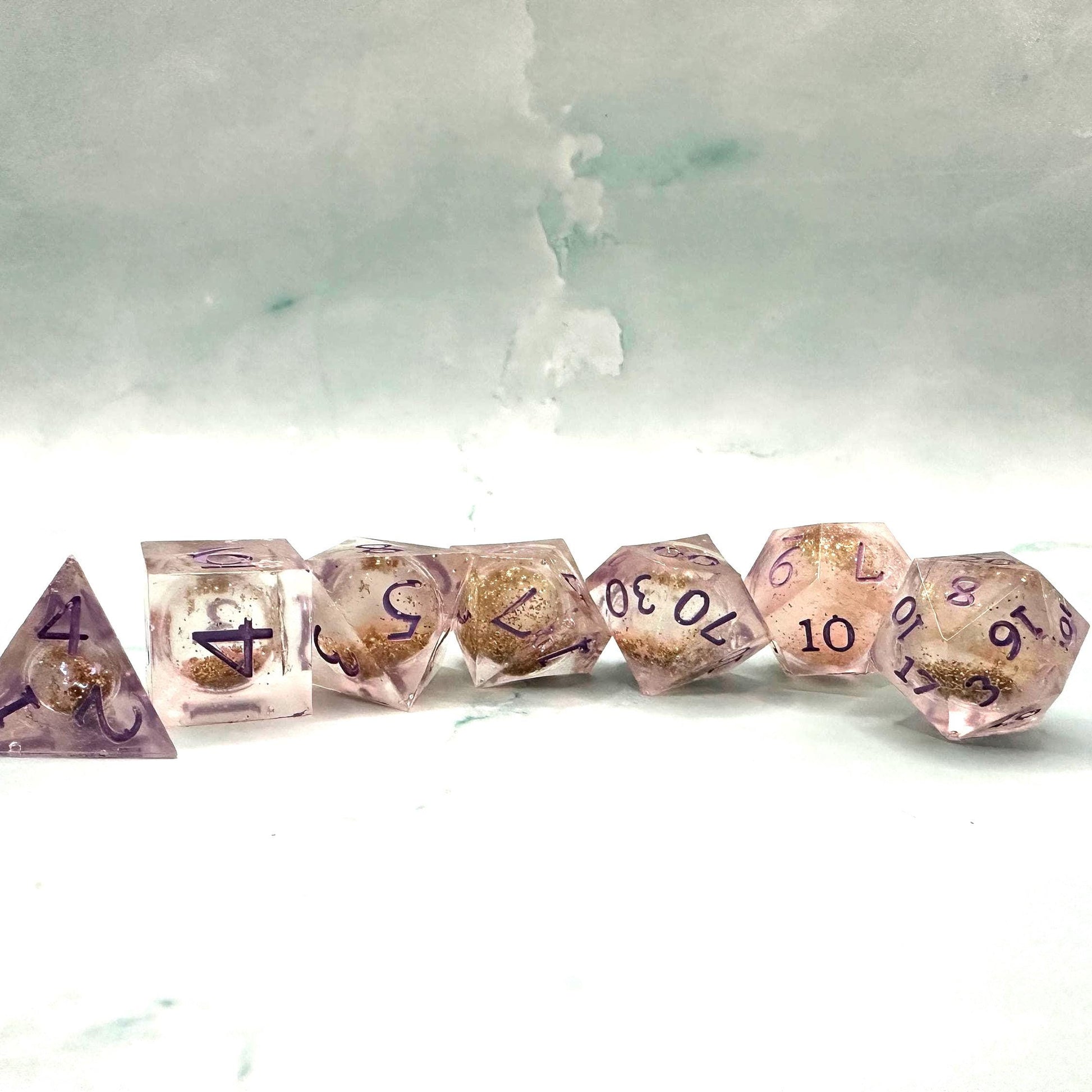 Light purple, pink, and gold glitter liquid core dice set shimmering with swirling metallic sparkle. Handcrafted polyhedral resin dice filled with floating glitter and vibrant liquid core for mesmerizing movement. Perfect for Dungeons & Dragons, tabletop RPGs, and dice collectors. Elegant pastel tones with gold accents add a magical, fantasy-inspired aesthetic for gaming sessions or gift giving.