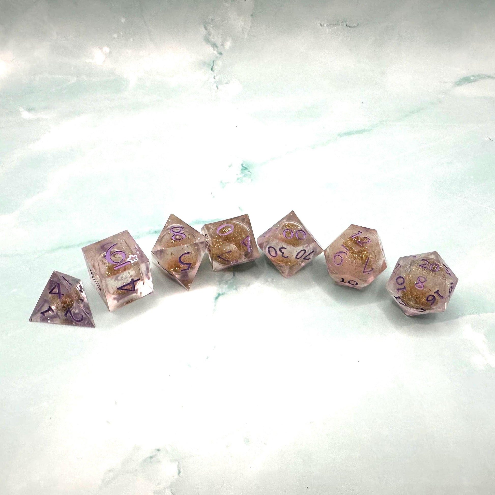 Light purple, pink, and gold glitter liquid core dice set shimmering with swirling metallic sparkle. Handcrafted polyhedral resin dice filled with floating glitter and vibrant liquid core for mesmerizing movement. Perfect for Dungeons & Dragons, tabletop RPGs, and dice collectors. Elegant pastel tones with gold accents add a magical, fantasy-inspired aesthetic for gaming sessions or gift giving.