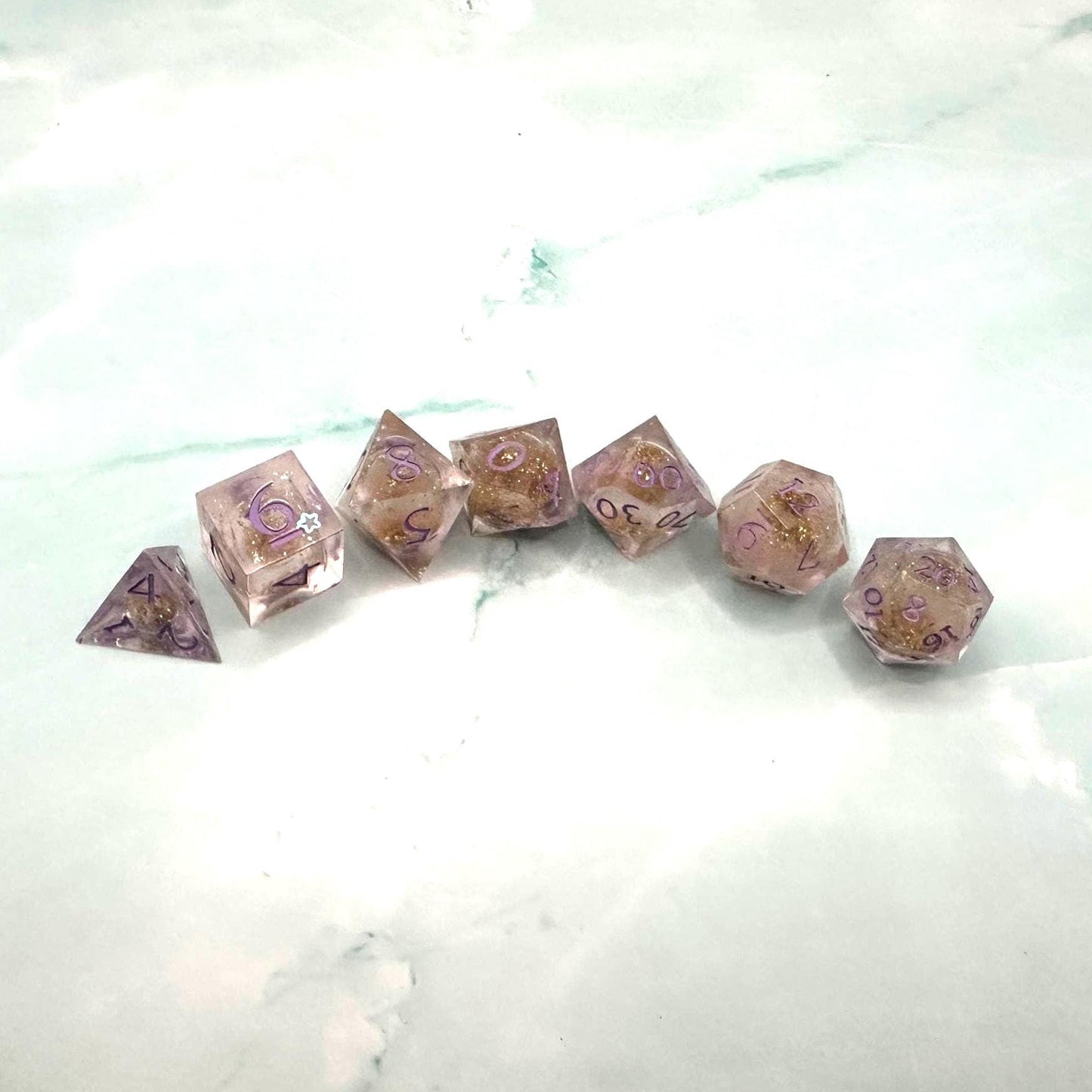 Light purple, pink, and gold glitter liquid core dice set shimmering with swirling metallic sparkle. Handcrafted polyhedral resin dice filled with floating glitter and vibrant liquid core for mesmerizing movement. Perfect for Dungeons & Dragons, tabletop RPGs, and dice collectors. Elegant pastel tones with gold accents add a magical, fantasy-inspired aesthetic for gaming sessions or gift giving.