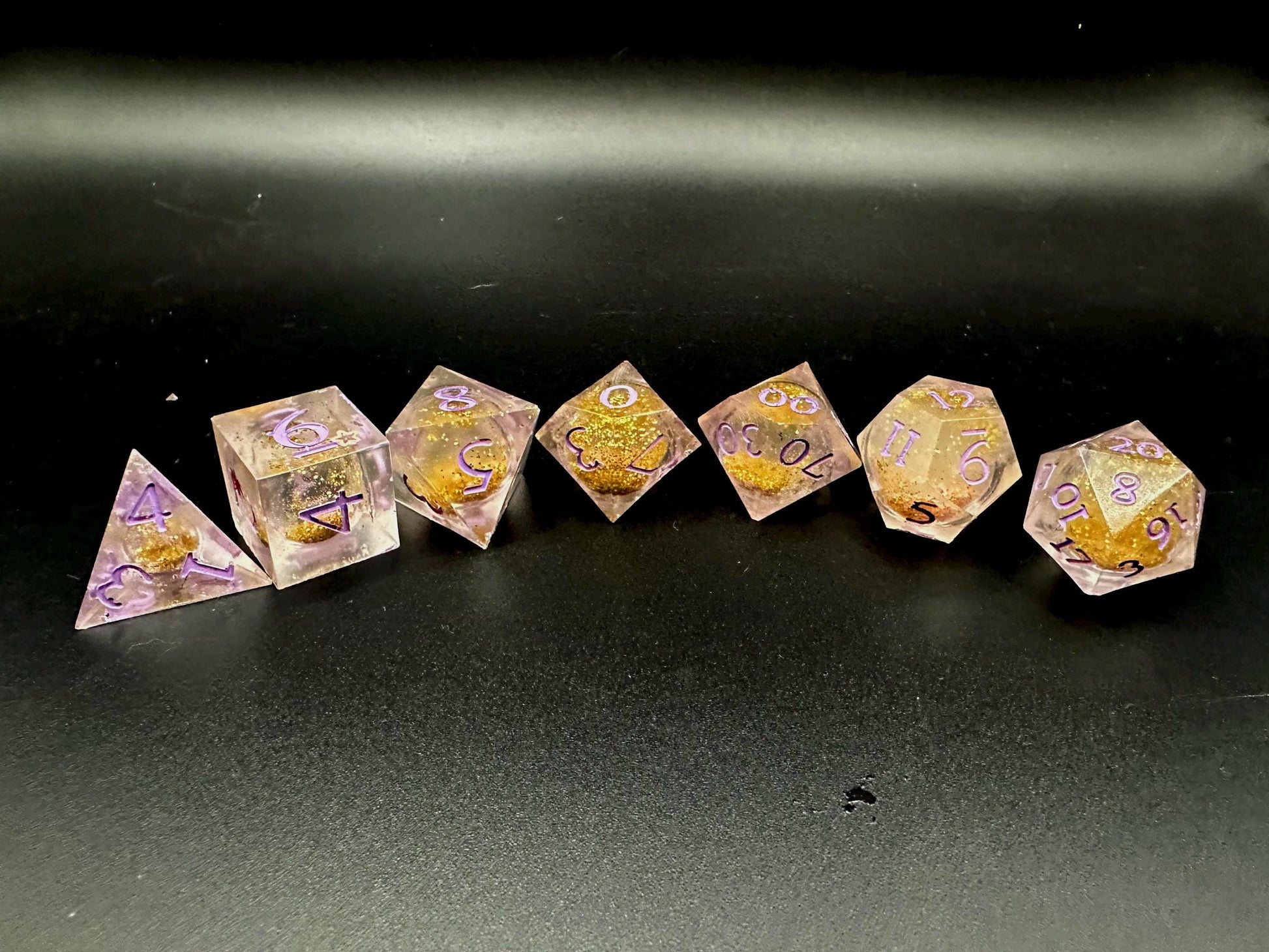 Light purple, pink, and gold glitter liquid core dice set shimmering with swirling metallic sparkle. Handcrafted polyhedral resin dice filled with floating glitter and vibrant liquid core for mesmerizing movement. Perfect for Dungeons & Dragons, tabletop RPGs, and dice collectors. Elegant pastel tones with gold accents add a magical, fantasy-inspired aesthetic for gaming sessions or gift giving.